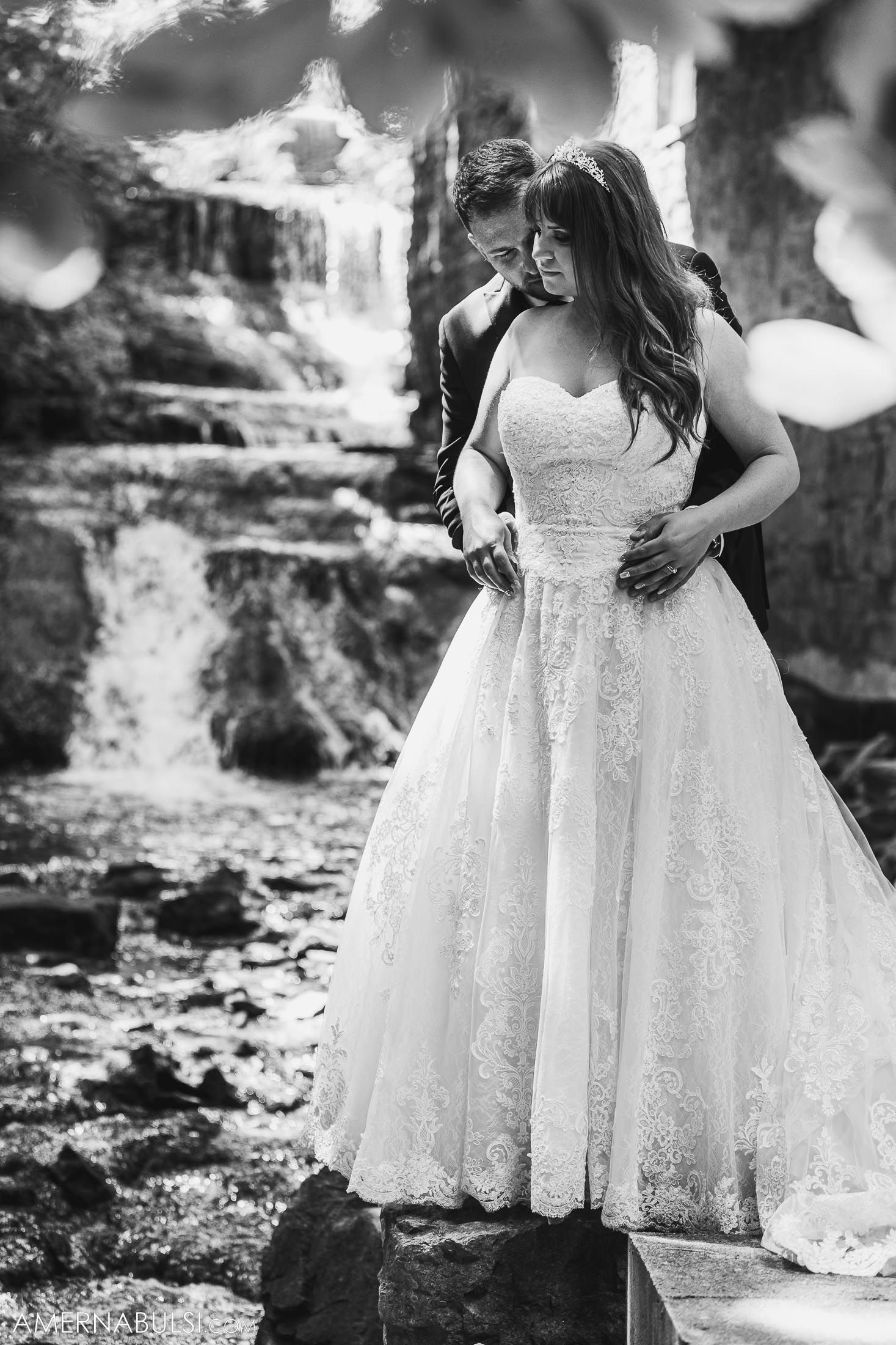 Black and white portrait of bride in lace gown by cascading waterfall.