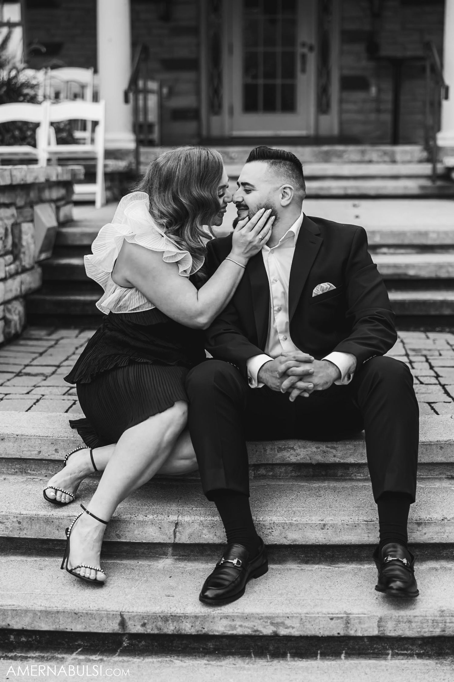 A couple shares an intimate moment while sitting on stone steps outdoors.