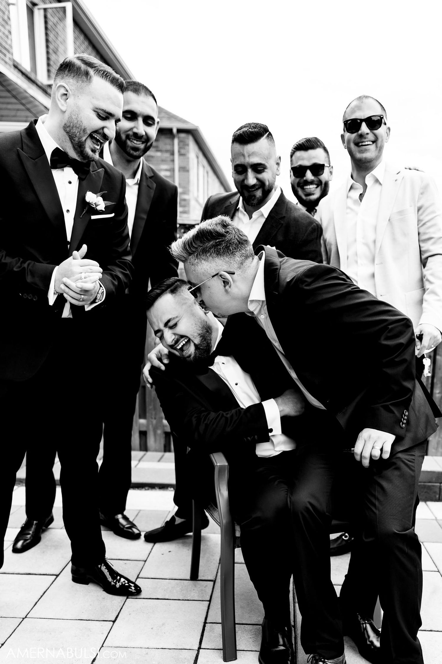 Black and white photo of groomsmen laughing and joking around during wedding photoshoot.