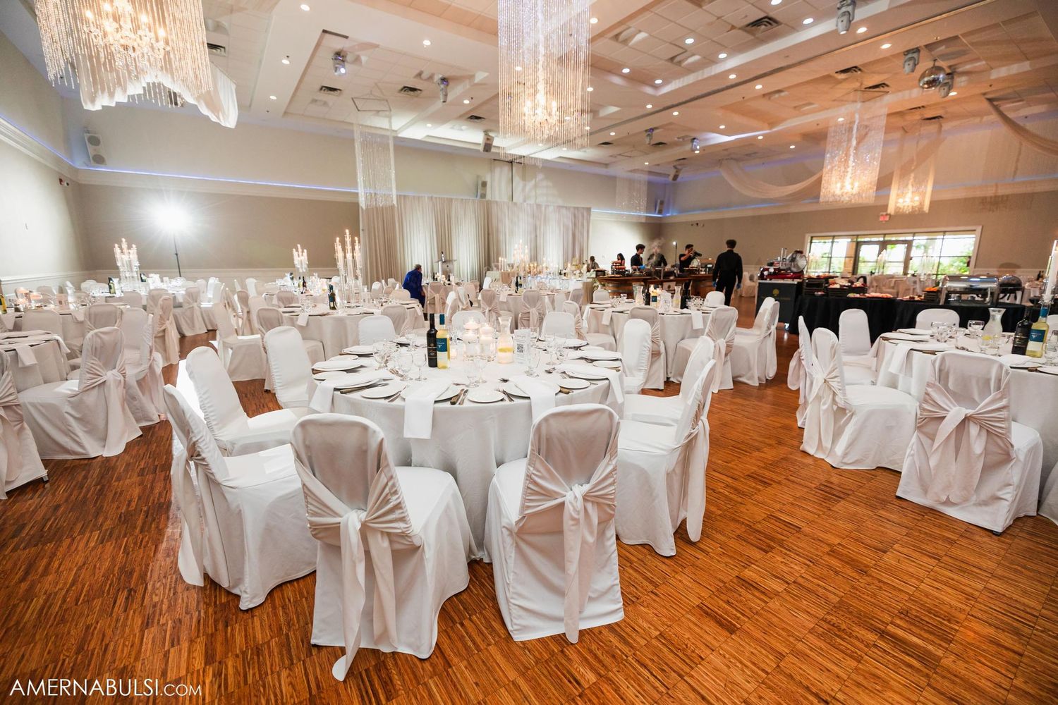 Elegant ballroom with white chair covers and crystal chandeliers set for wedding reception.