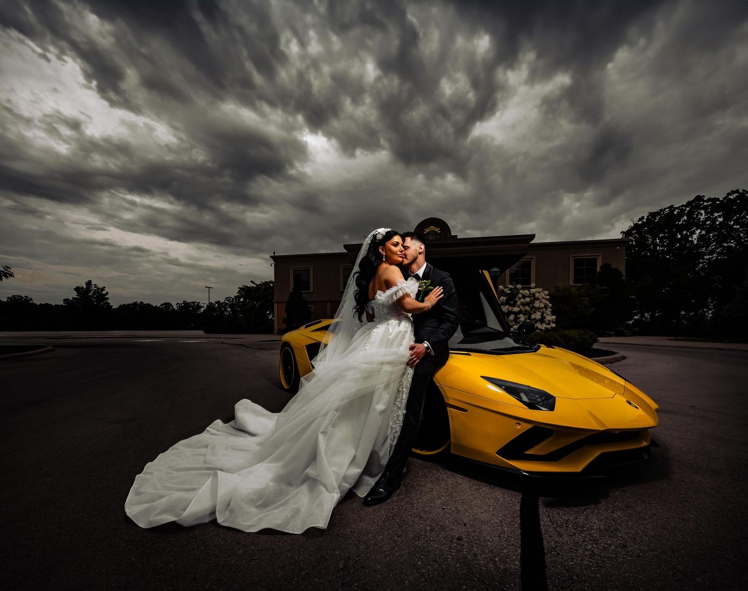Dramatic wedding photo with couple posing against yellow Lamborghini under stormy sky.