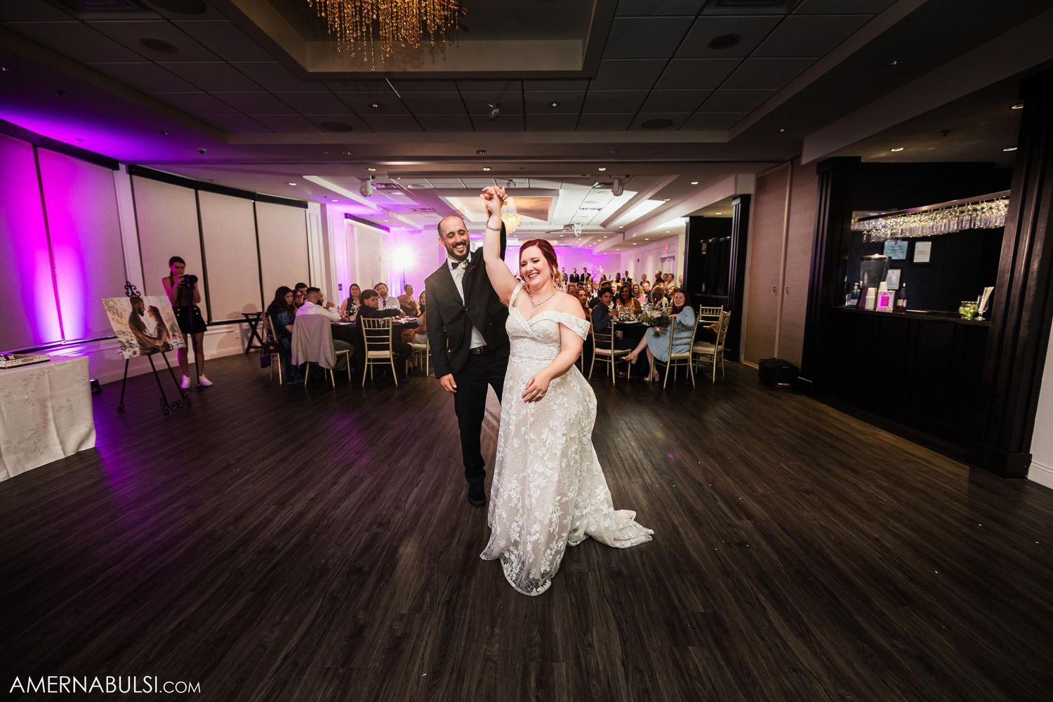Couple dancing together on wooden floor with purple lighting at wedding reception.