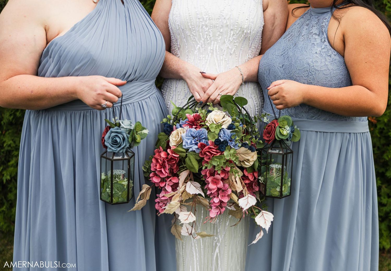 Close-up of bridesmaids in blue dresses holding floral bouquets and lanterns.