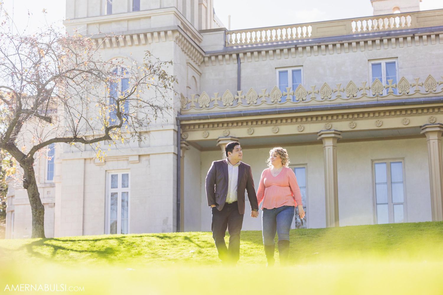 Couple walking hand in hand near stately mansion with spring foliage in foreground.