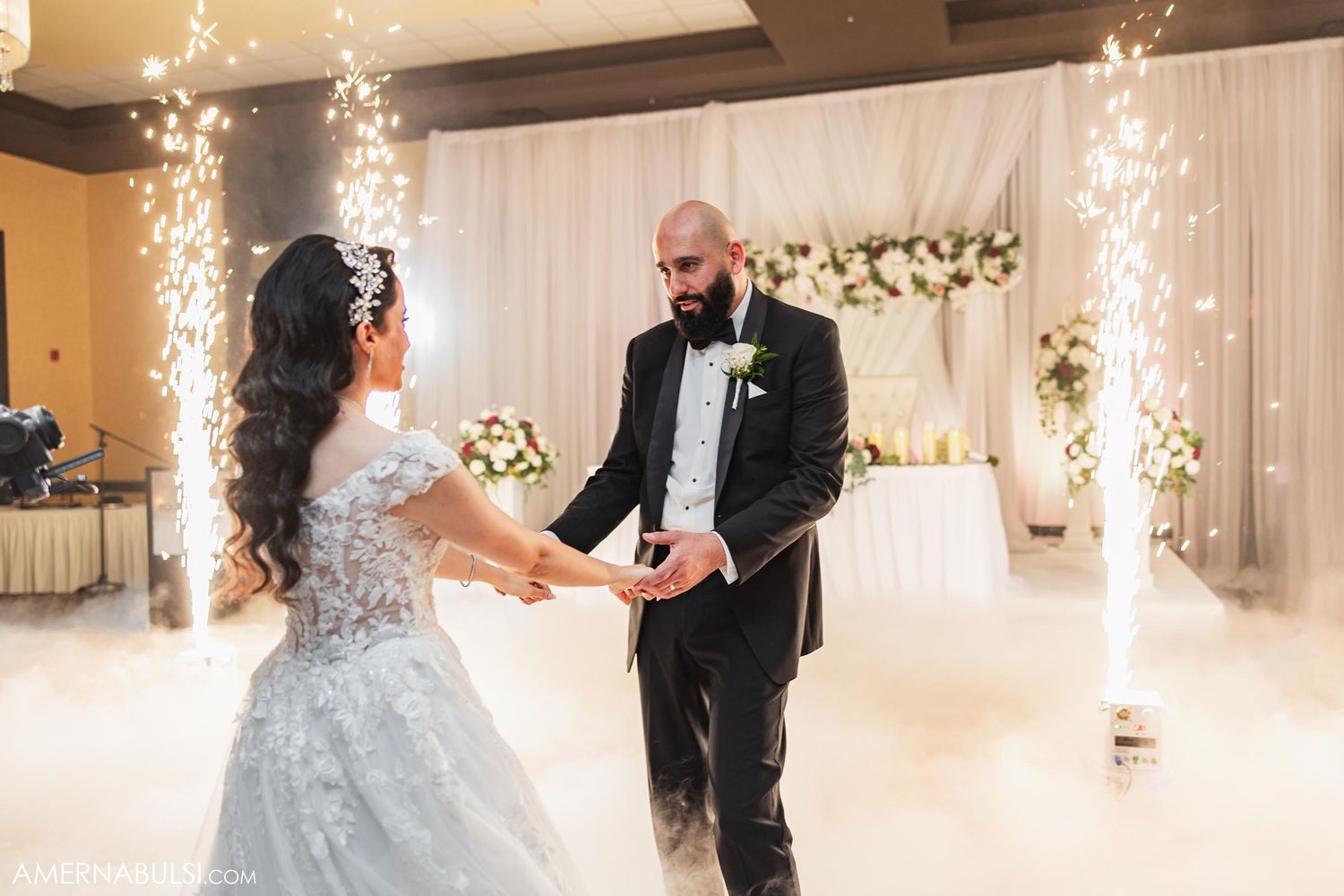 A couple dances during their wedding reception with sparkling lights and floral decorations.