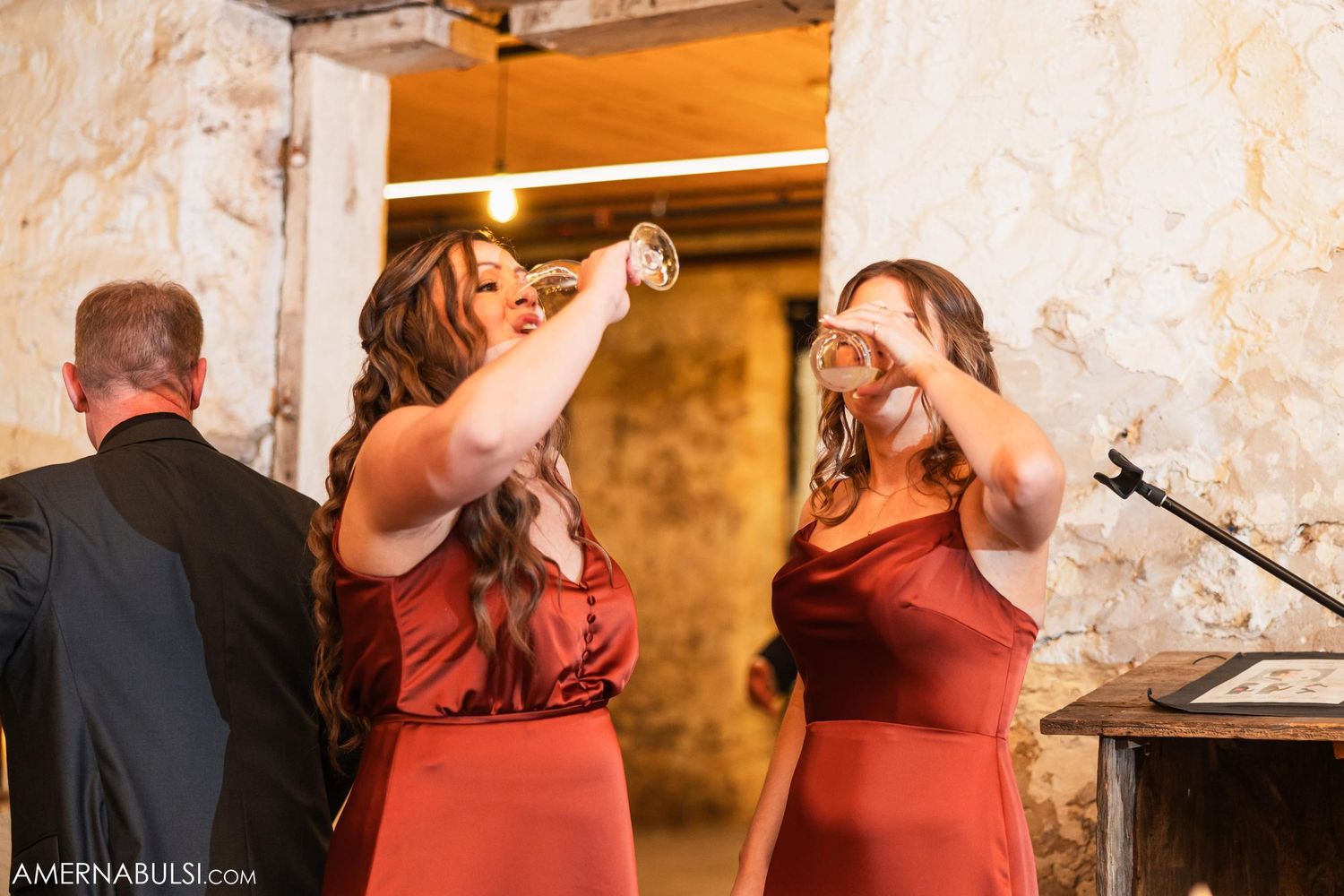Bridesmaids in burgundy dresses toast during wedding reception celebrations.