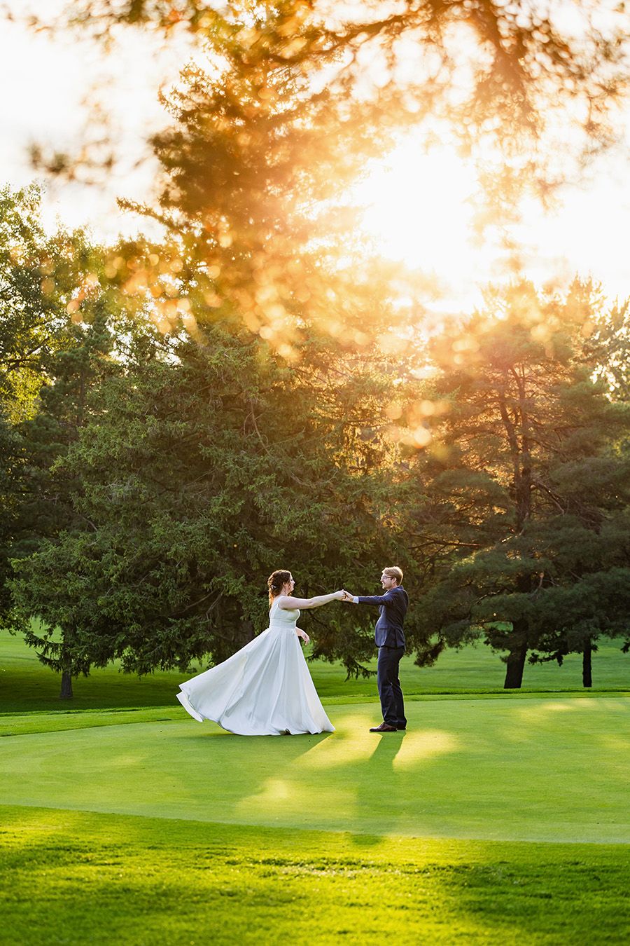 Newlyweds dance together on a lush green golf course at golden sunset.