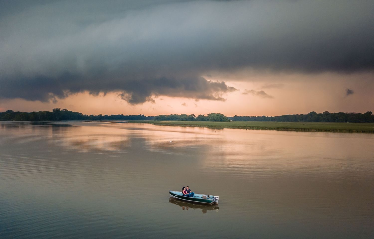 Moody sunset over calm waters with silhouette of small boat in the distance.