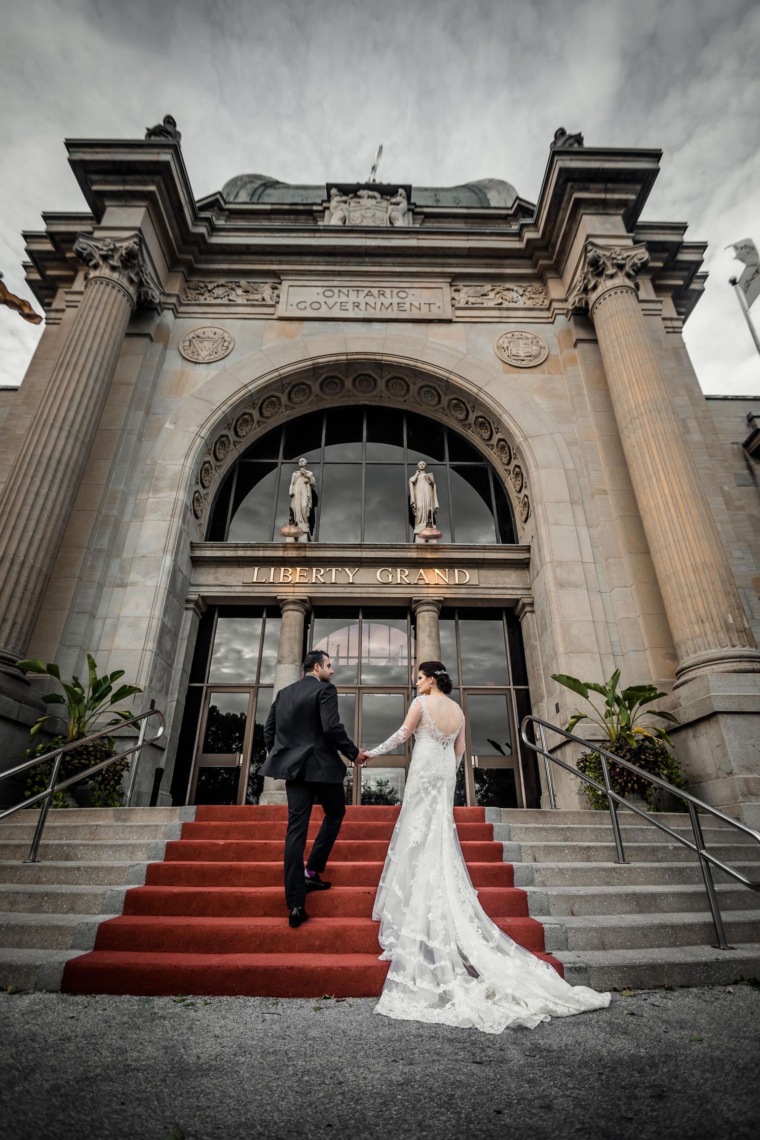Elegant couple ascending grand stone steps with red carpet at historic building entrance.