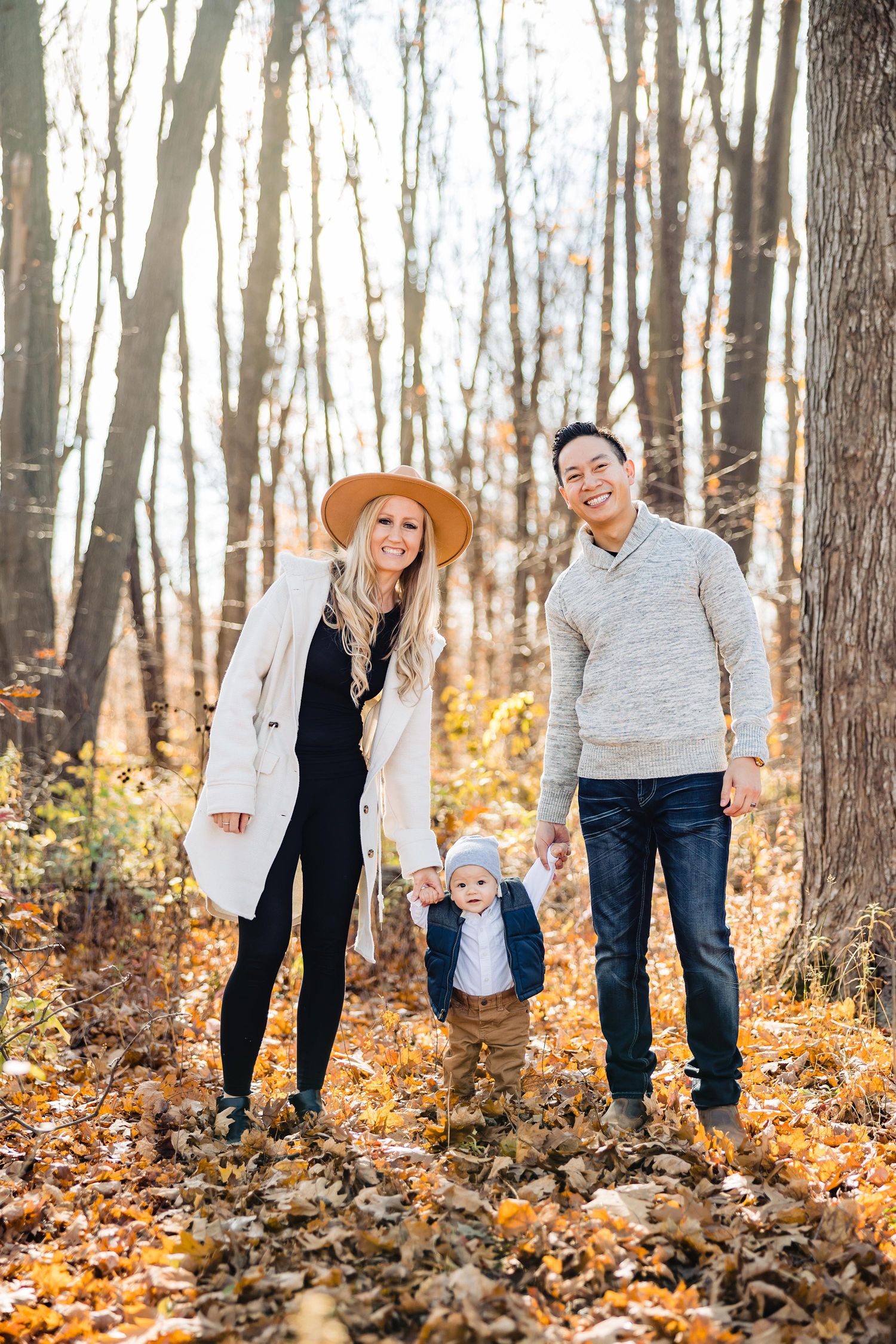 A family plays together in a forest filled with fallen autumn leaves on a bright sunny day.