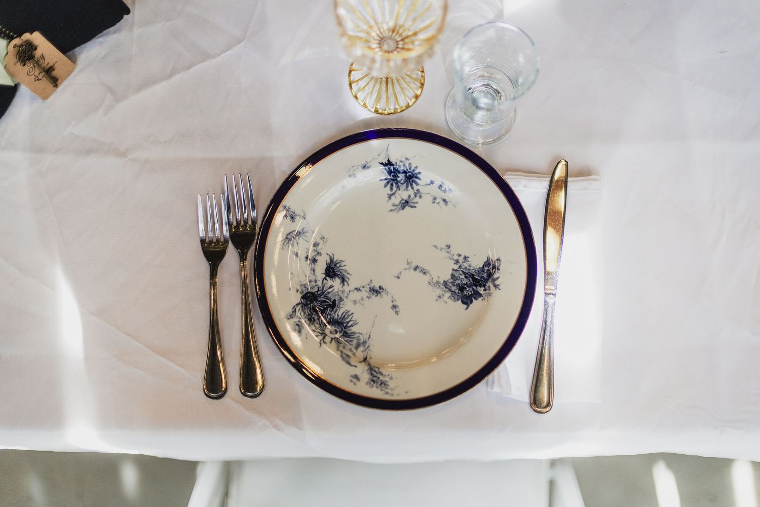 Classic blue and white floral china plate with gold silverware on white tablecloth.