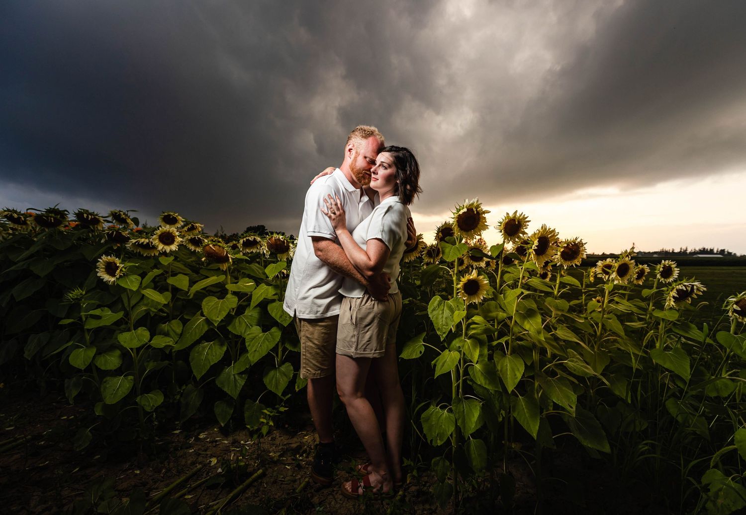 Dramatic sunset engagement photos in field of sunflowers with stormy sky backdrop.