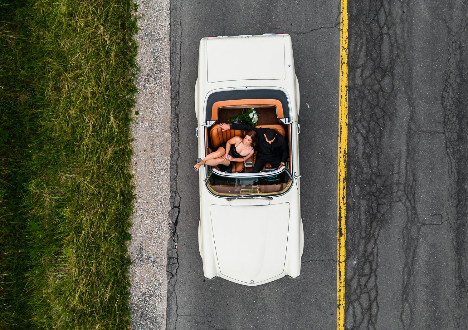 Aerial view of vintage white car driving on asphalt road with yellow line.