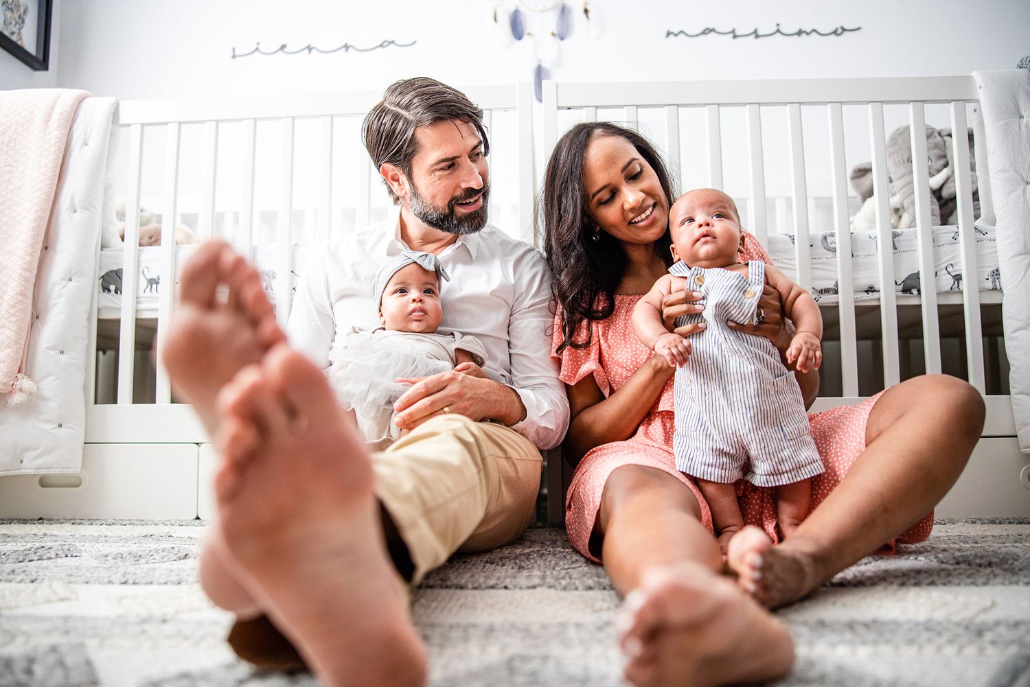 Family members relax together on a white bed, sharing playful moments and laughter in casual indoor setting.