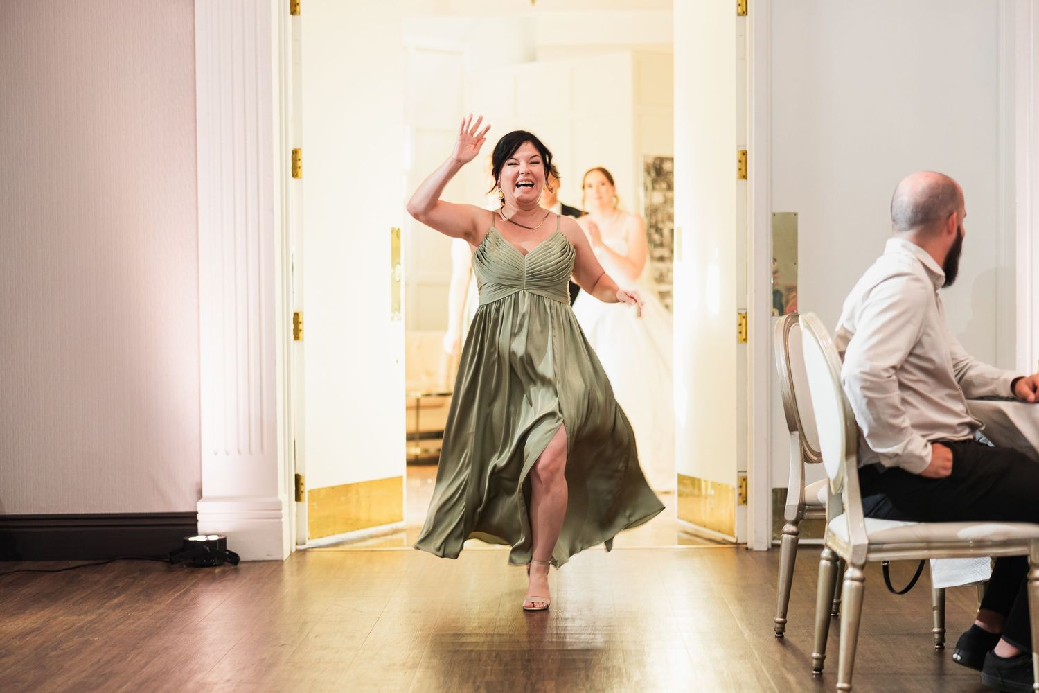 Woman in green dress dancing barefoot through doorway at wedding reception.