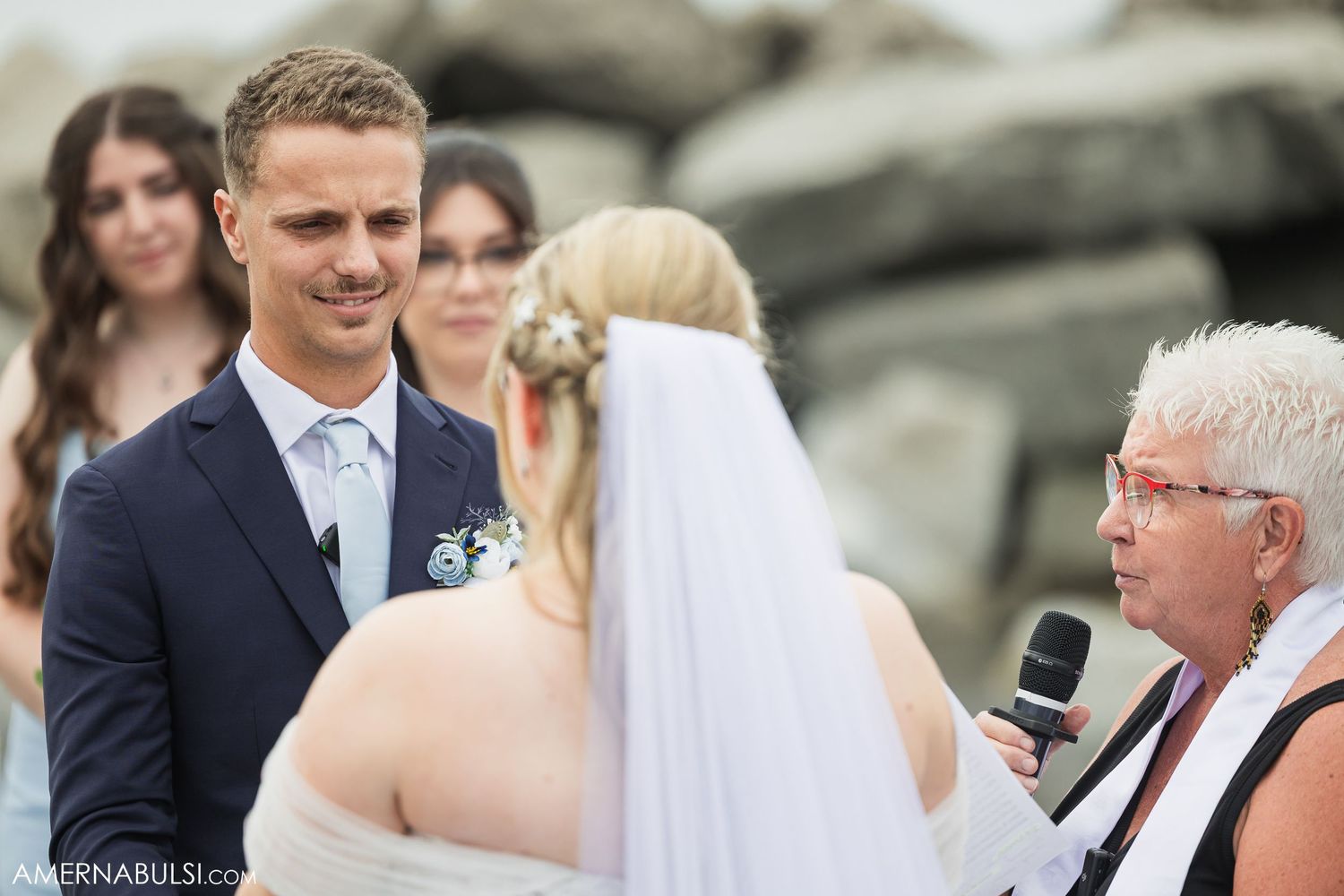 Guests observe a seaside wedding ceremony among rocky coastal outcroppings.