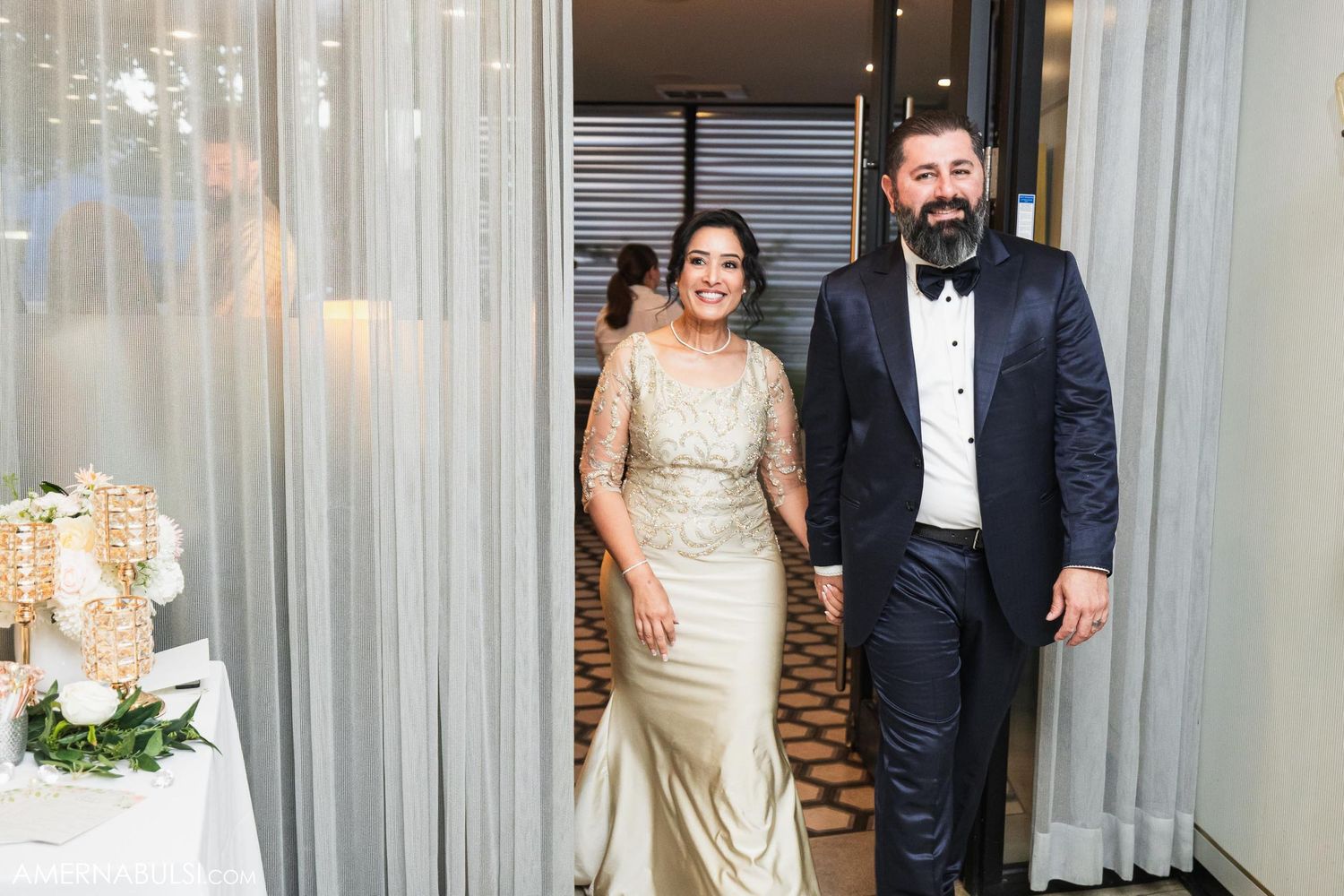 Elegant couple in formal wedding attire standing in modern venue hallway.