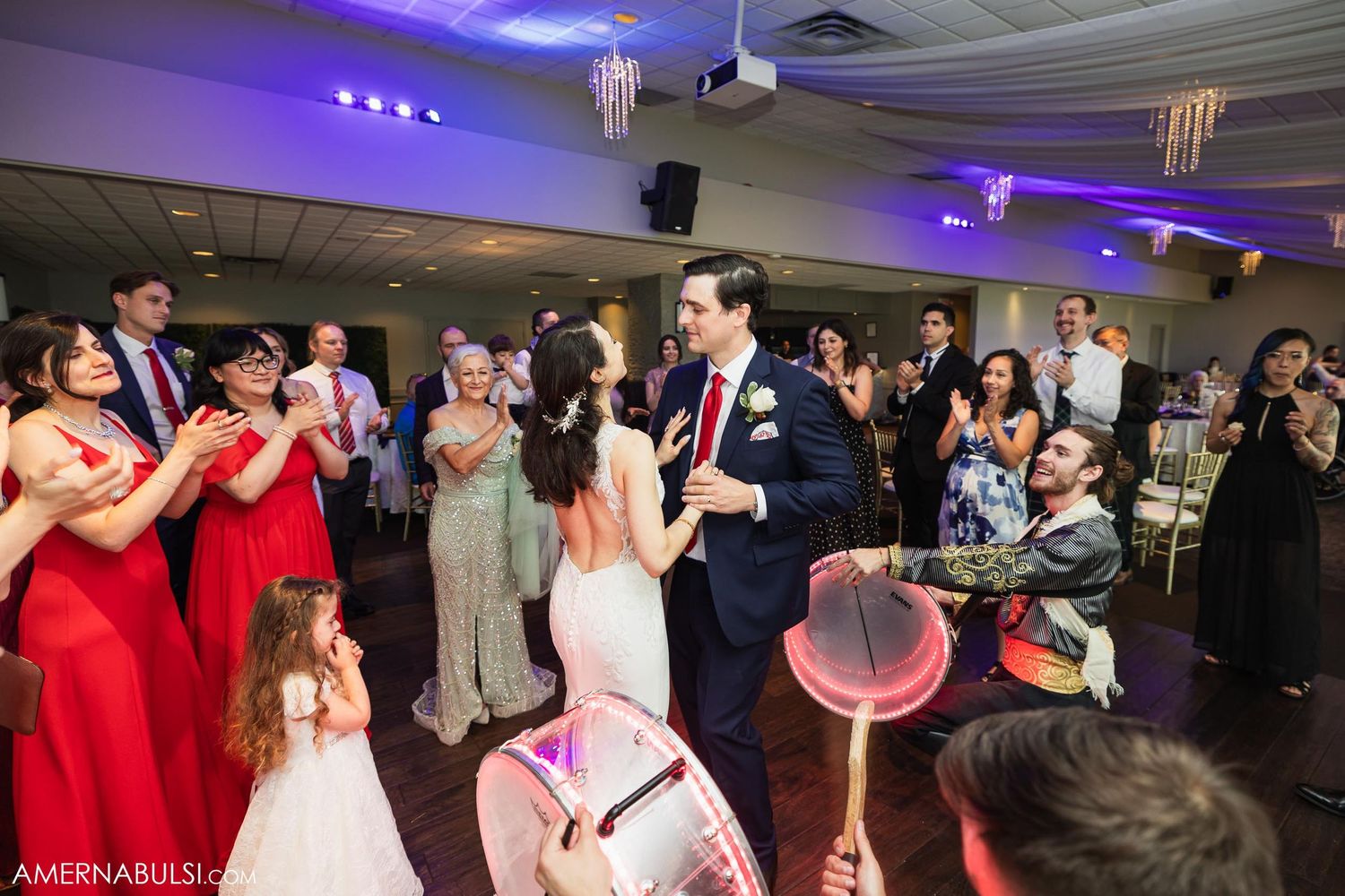 Wedding celebration on dance floor with guests in red dresses watching.
