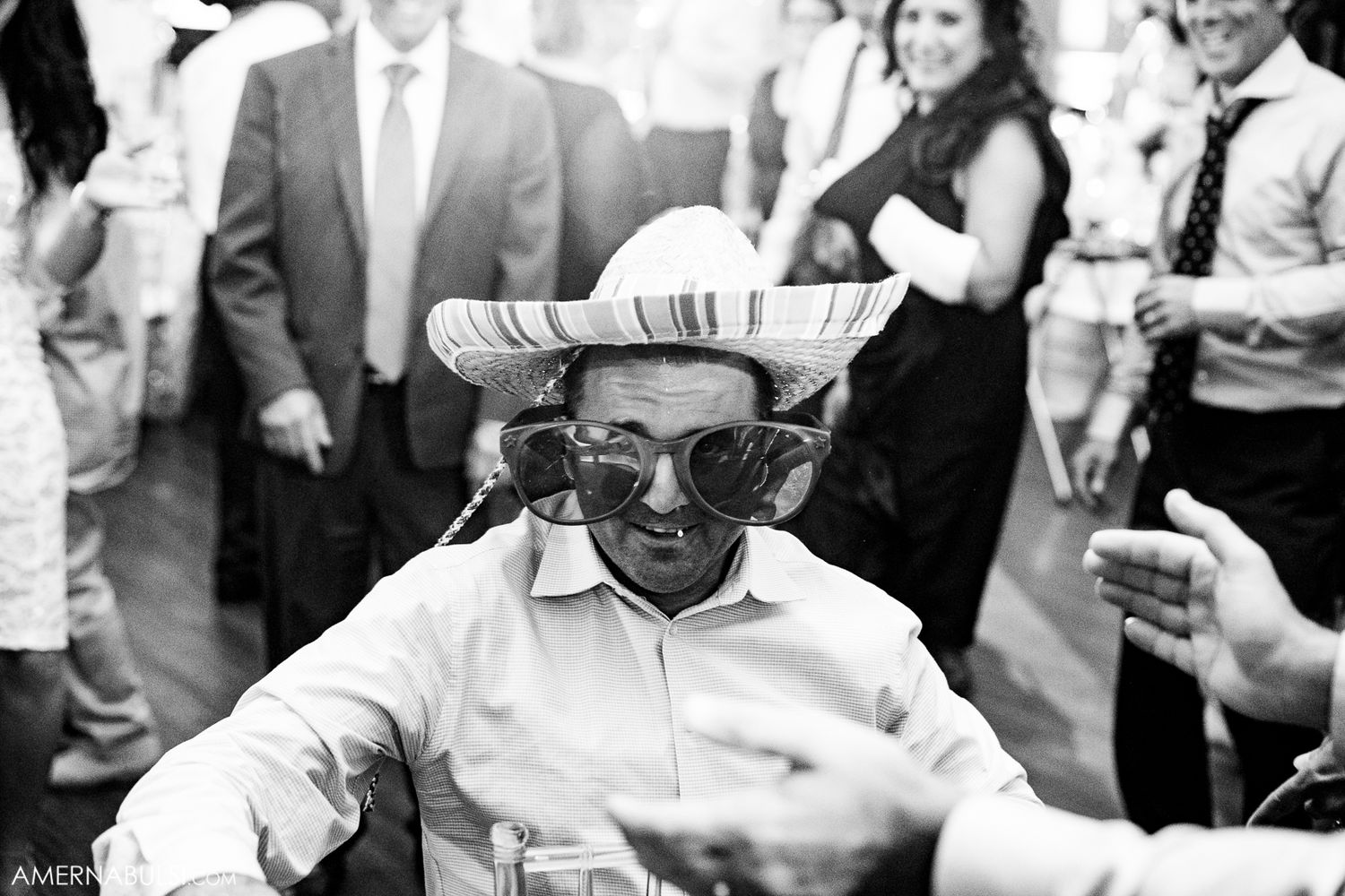 Black and white photo of wedding guests dancing and celebrating at an indoor reception venue.