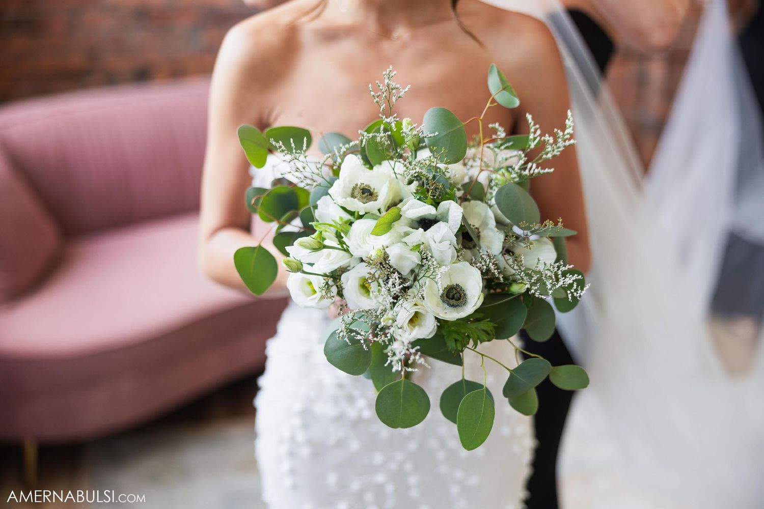 Close up of white floral wedding bouquet with eucalyptus leaves against bridal gown.