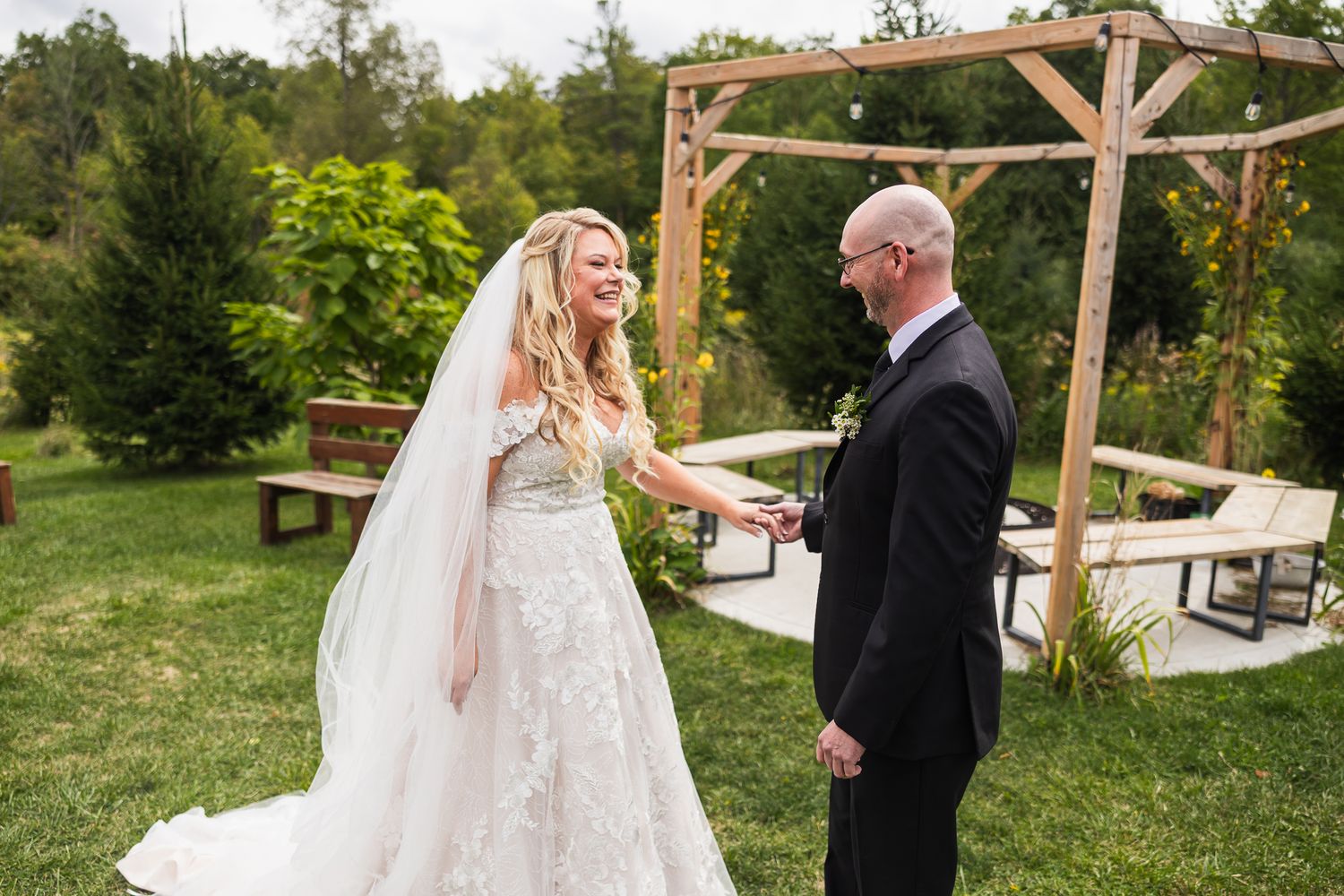 Bride and groom share joyful expressions during outdoor wedding ceremony beneath rustic wooden arch.