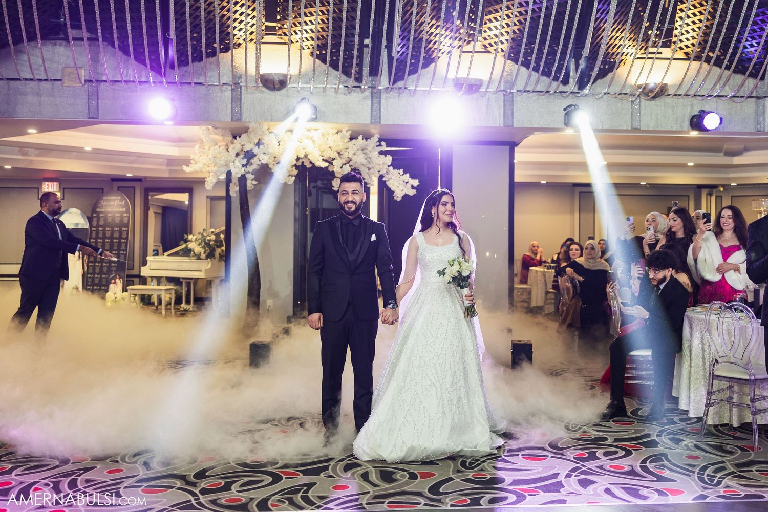 Wedding reception venue decorated with elegant white floral arrangements and purple uplighting for an evening celebration.