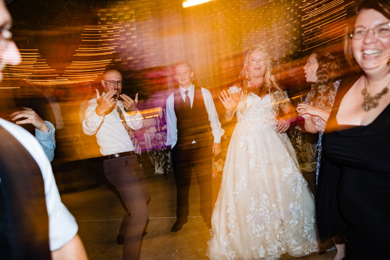 Partygoers dancing and celebrating at an indoor reception venue with warm amber lighting.