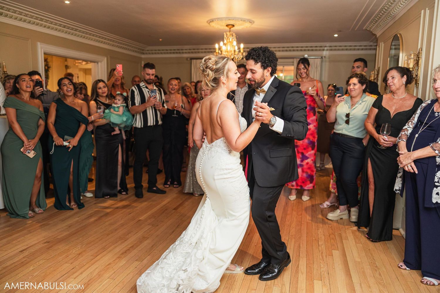 Wedding couple shares first dance surrounded by guests in formal attire.
