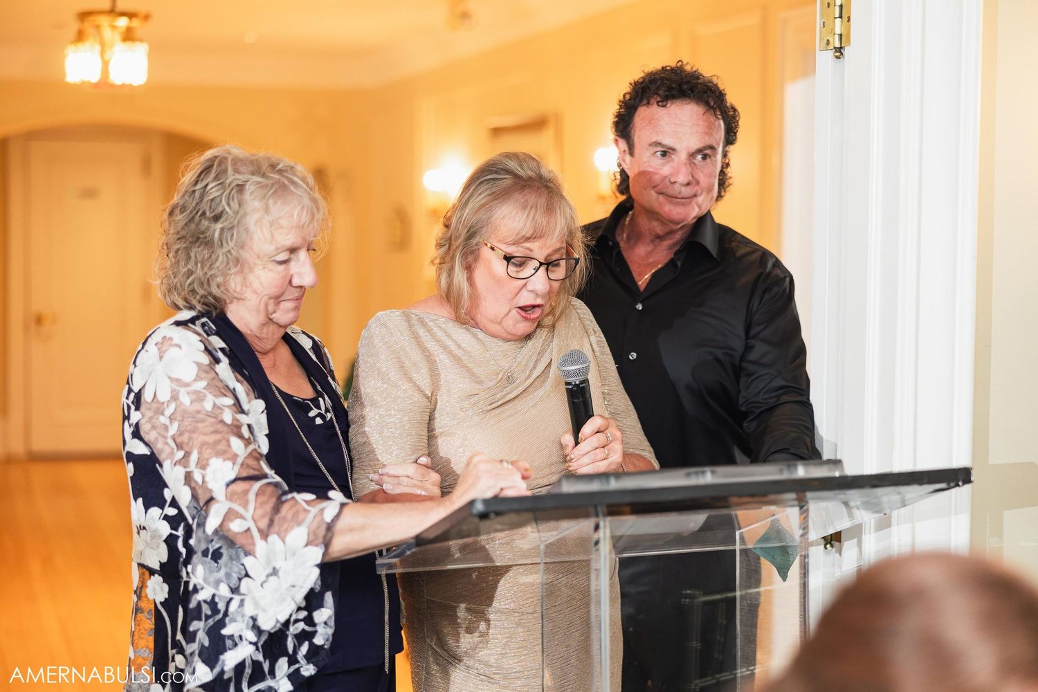 Three people gathered at a podium during a wedding reception speech.