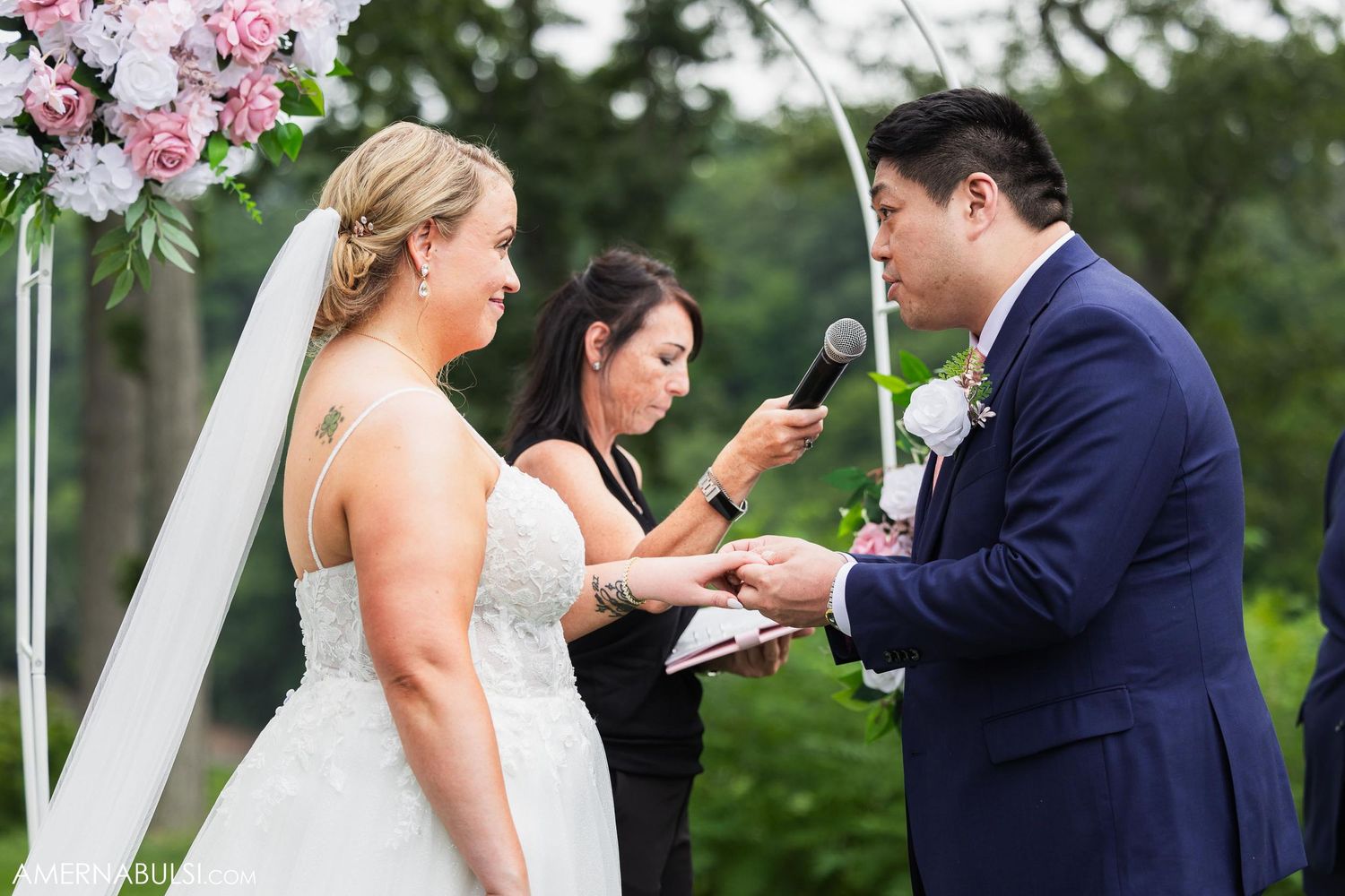 Wedding ceremony moment as officiant conducts vows under floral arch outdoors.