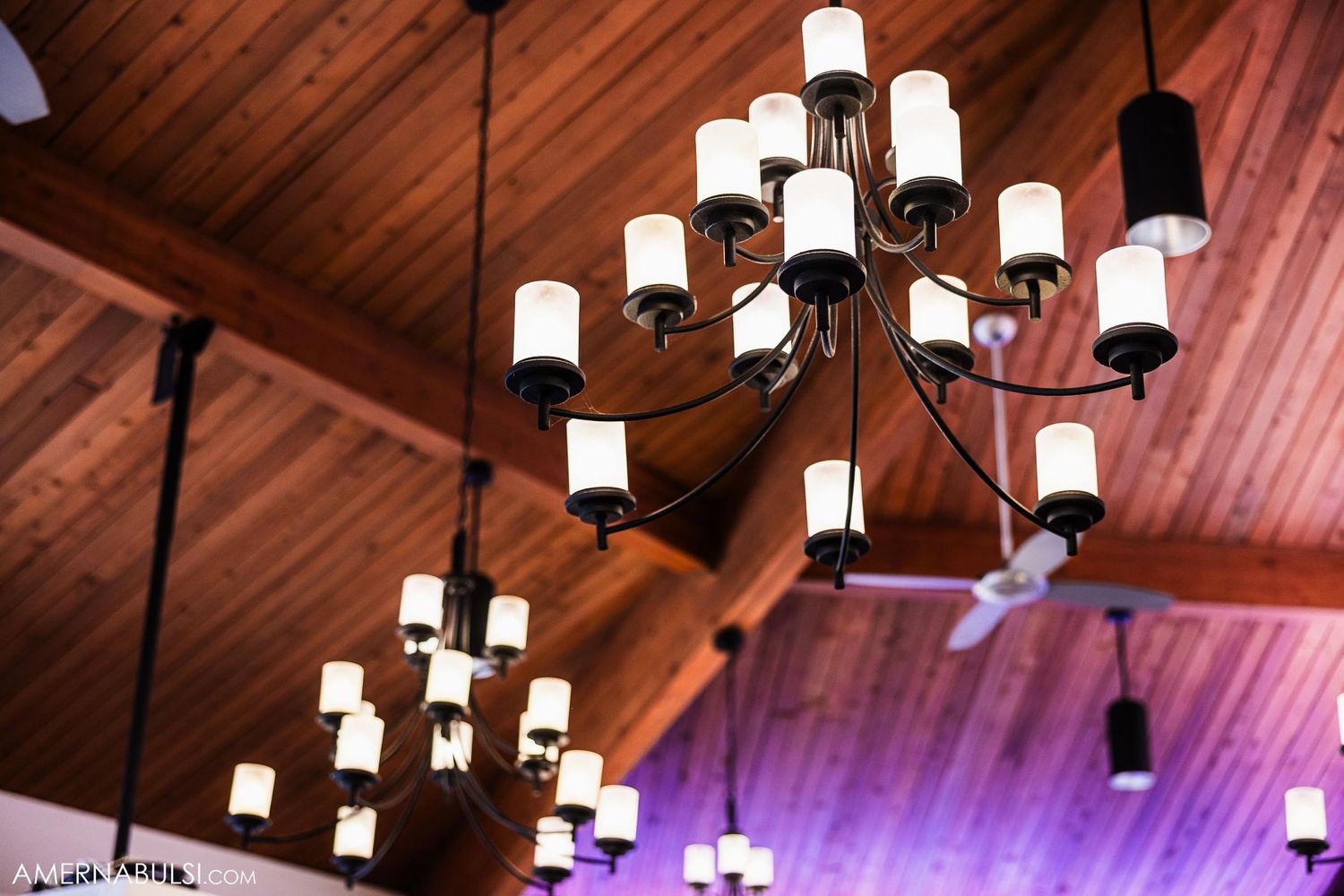 Modern chandelier with white glass lights hanging from wooden cathedral ceiling.