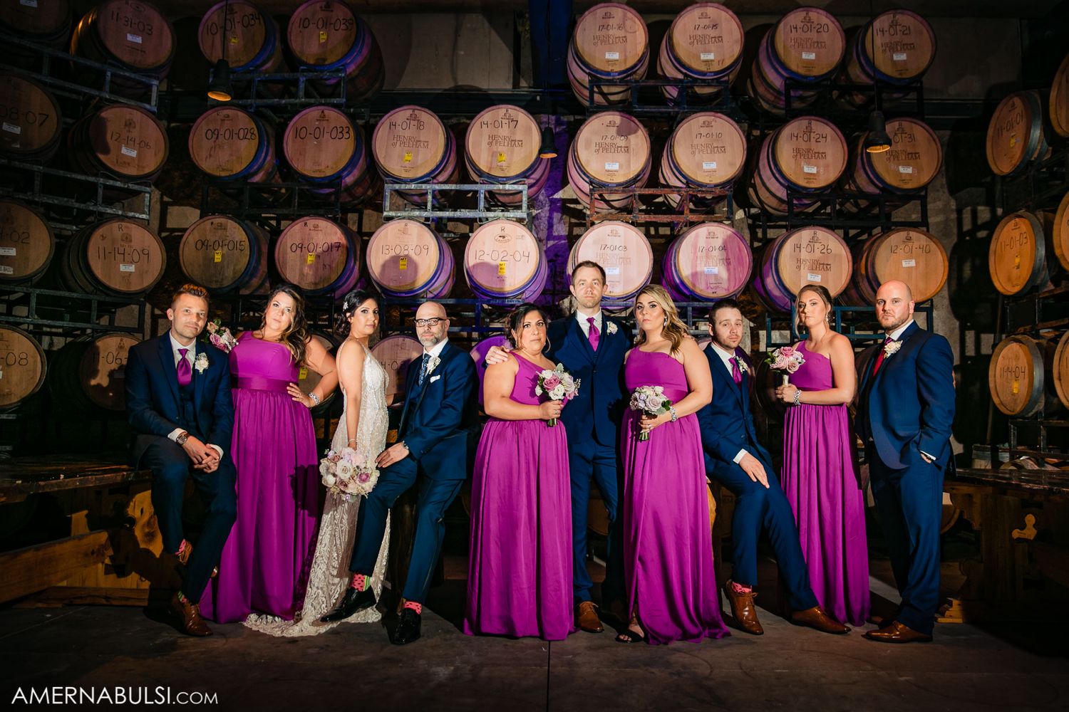 Wedding party poses in front of rustic wooden wine barrels in atmospheric lighting.