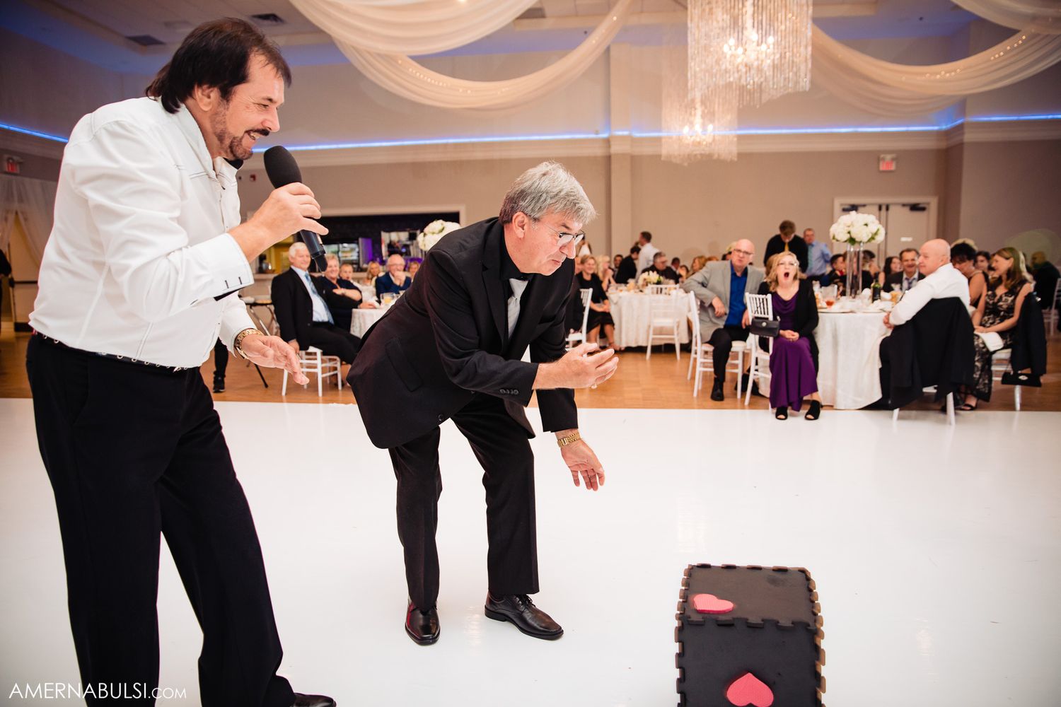 Wedding reception dance floor filled with guests enjoying the celebration under elegant draped fabric and chandeliers.