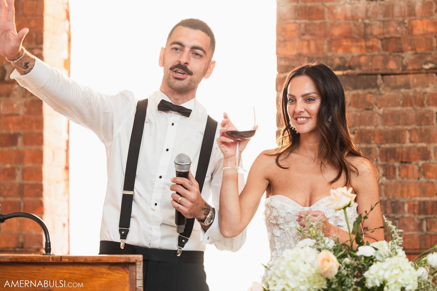 Celebratory toast moment with wine glasses in front of exposed brick wall.