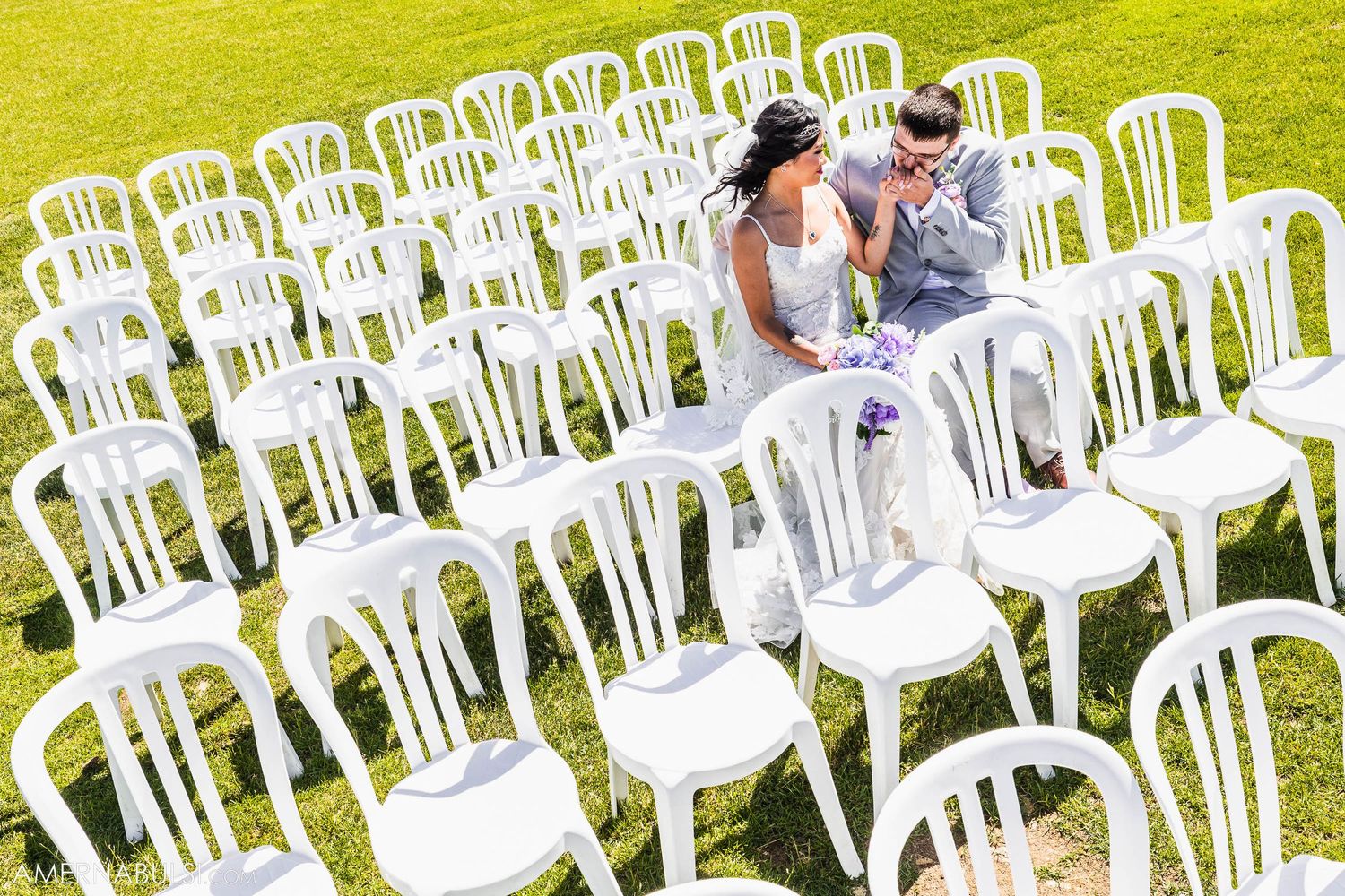 Outdoor wedding ceremony setup with rows of white chairs against a bright green lawn.