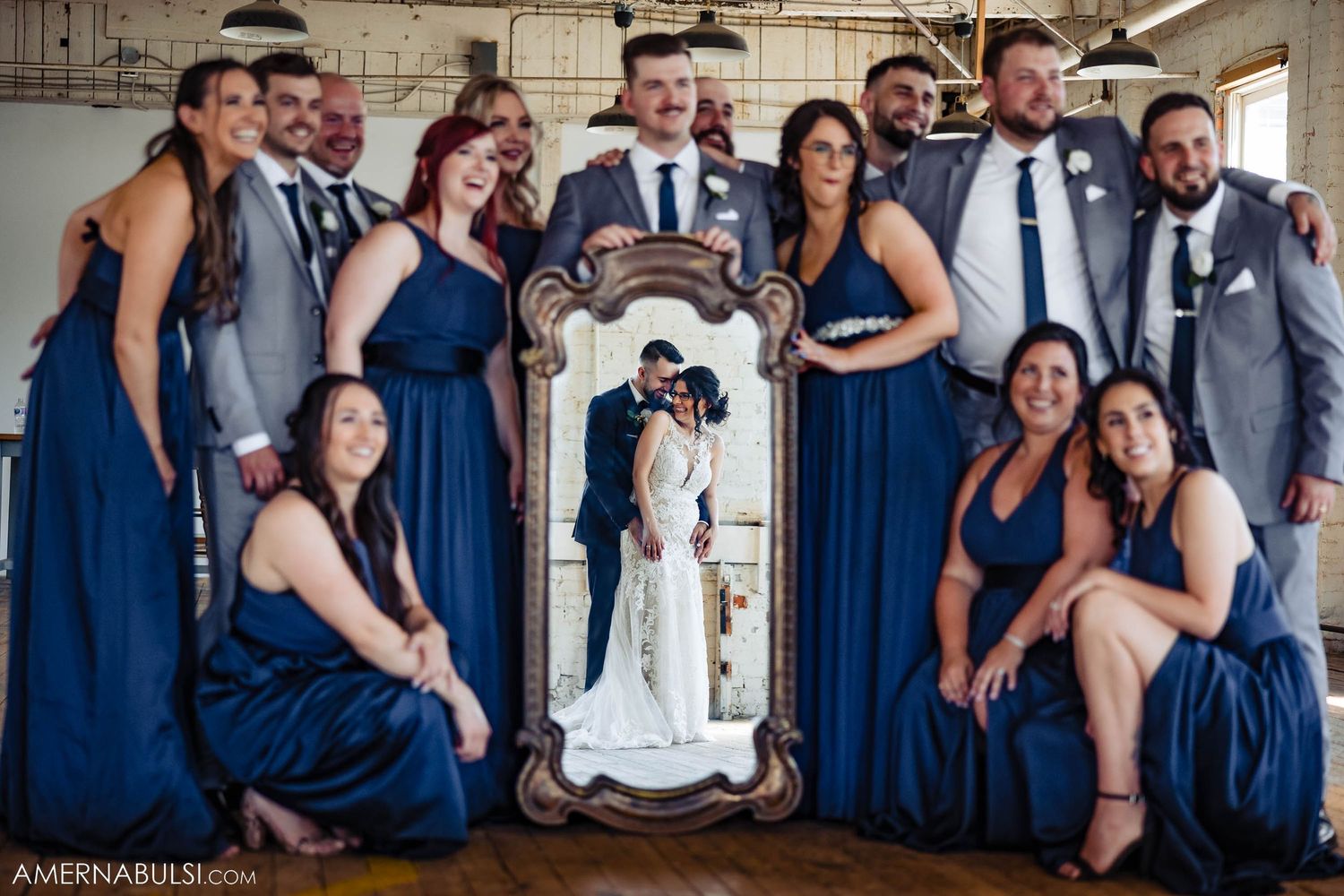 Wedding party in navy blue attire poses with a decorative mirror in an industrial venue.