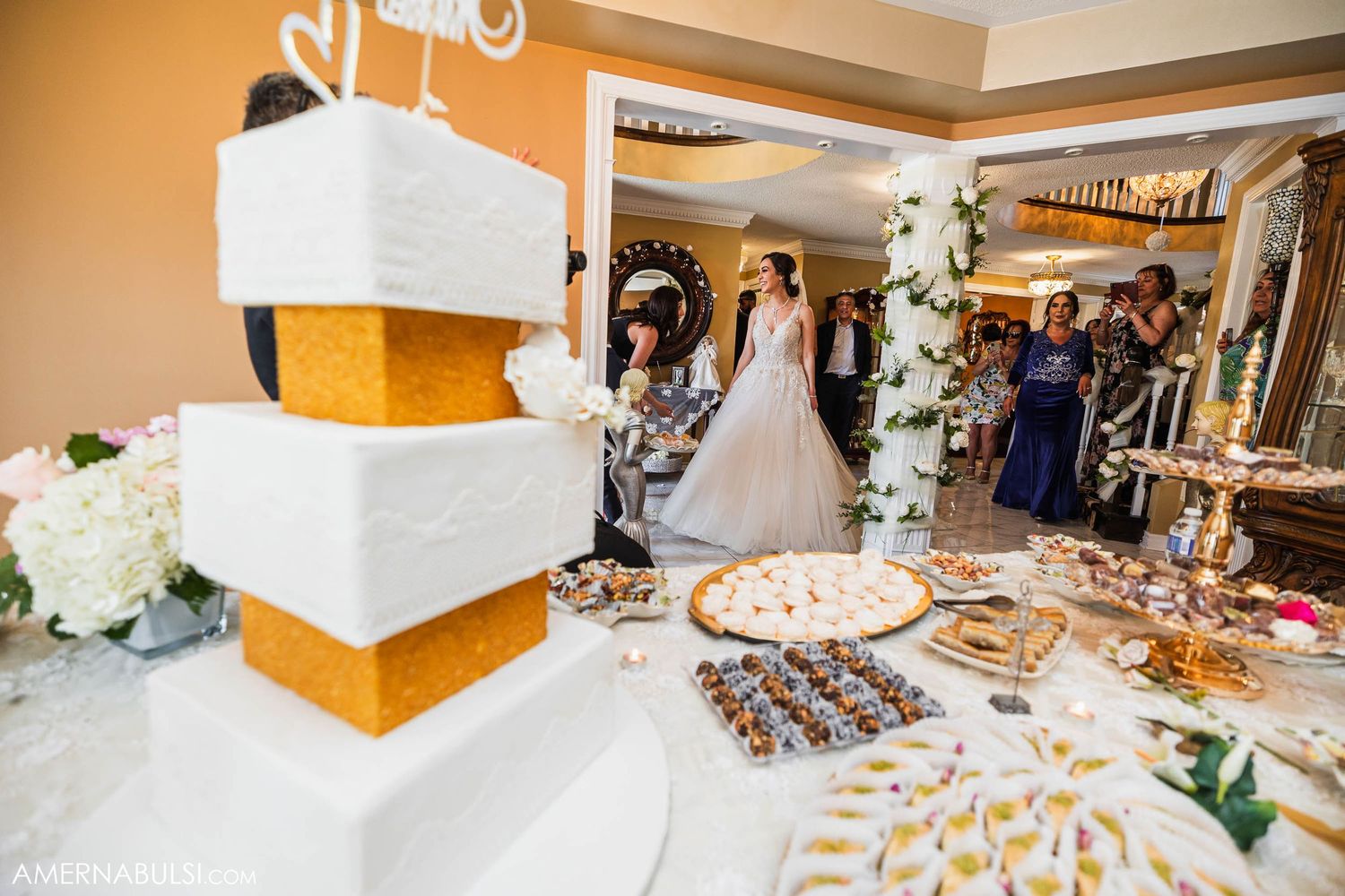 Elegant wedding dessert table with white tiered cake adorned with gold accents and floral decorations at reception.