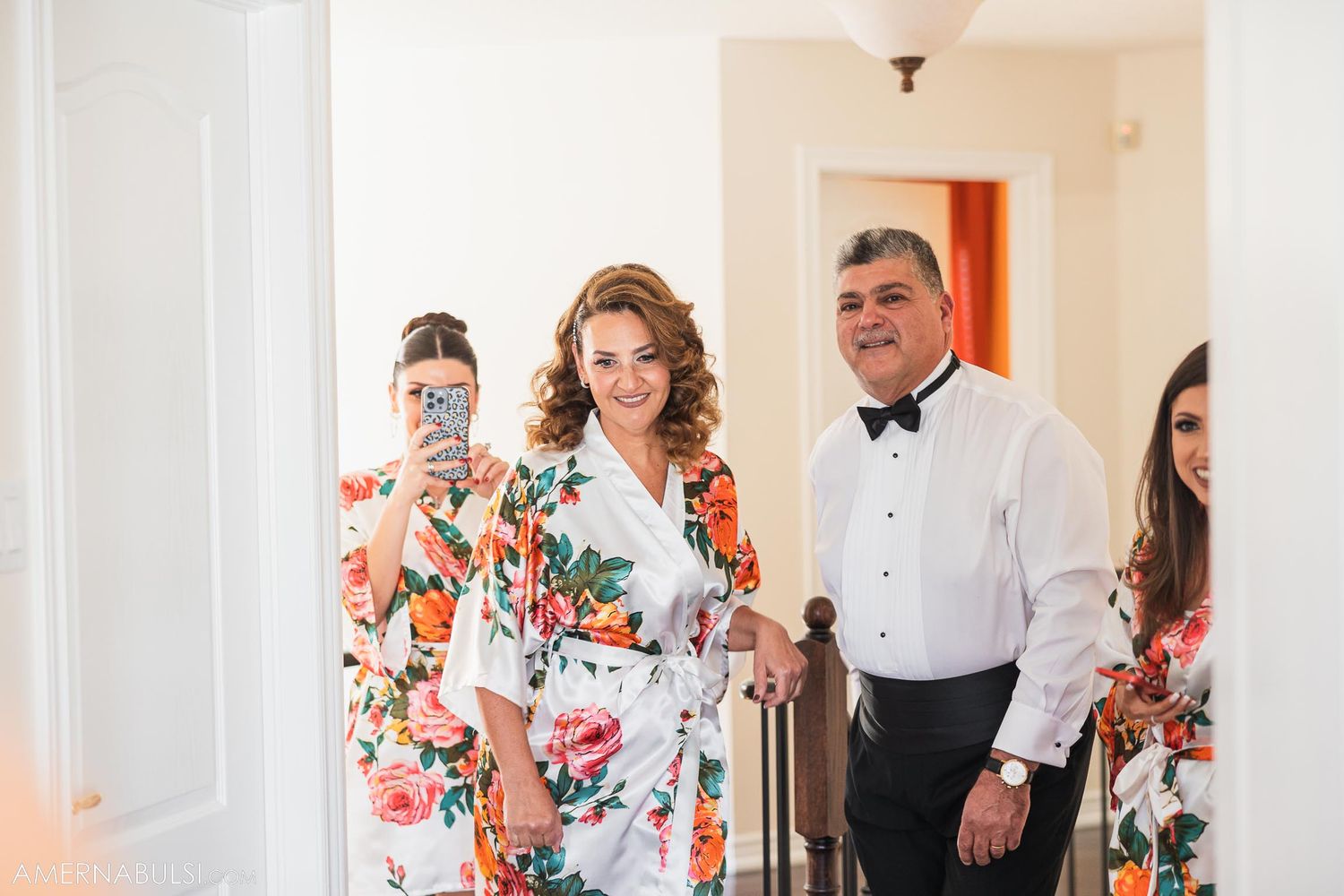 Wedding party members in floral robes and formal attire gather in a hallway.
