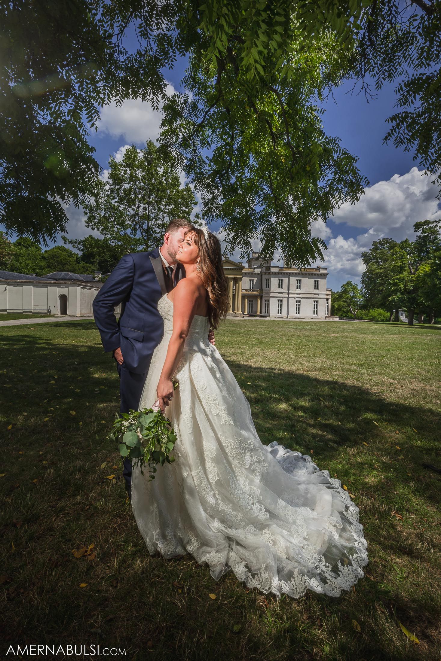 Romantic wedding portrait of a couple in formal attire posing on the lawn of a grand estate.