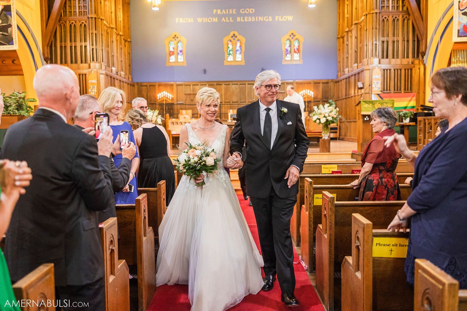 A wedding processional makes its way down a red-carpeted aisle in a traditional church setting.