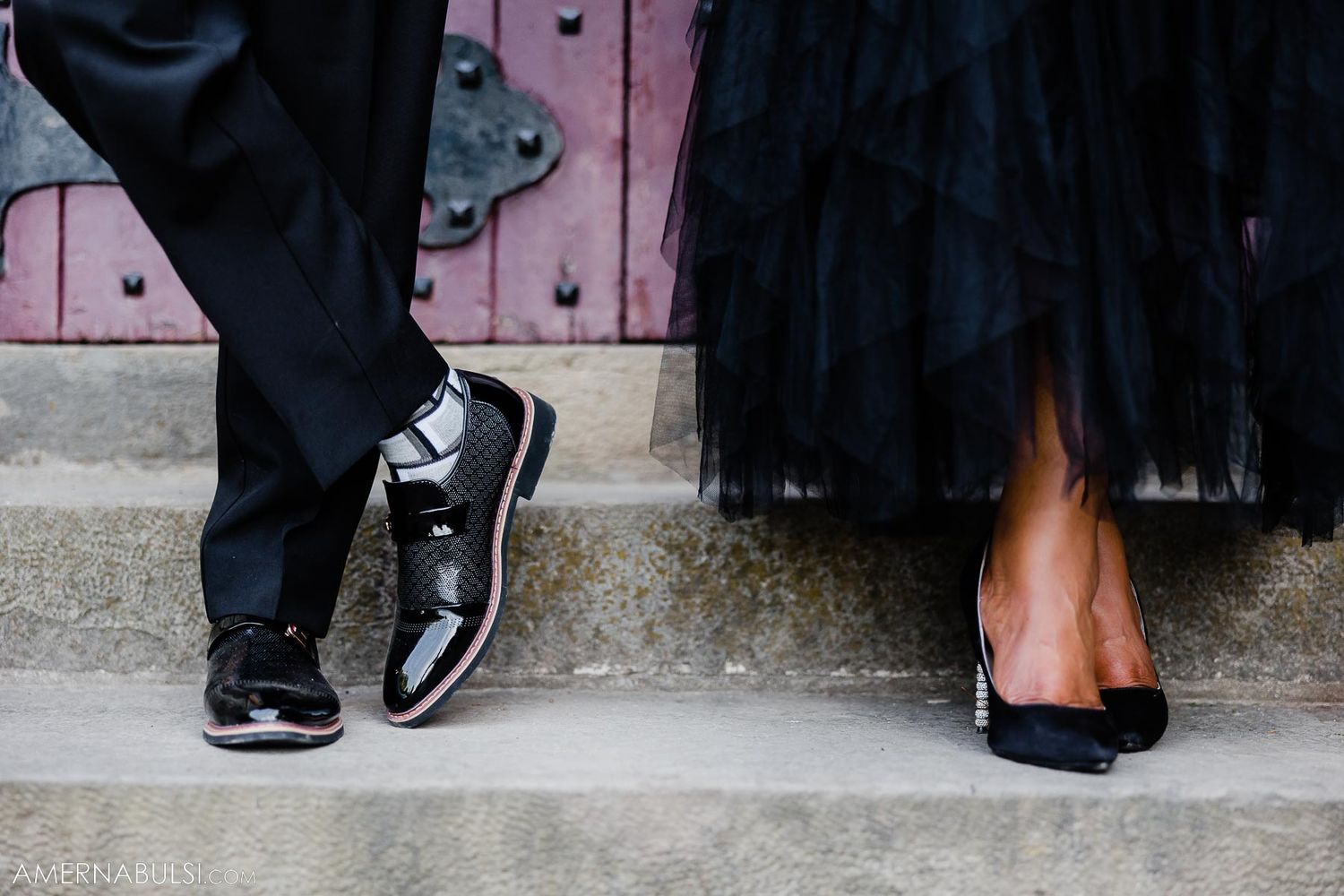 Close-up of couple's feet showing patent leather shoes and black tulle dress hem on stone steps.
