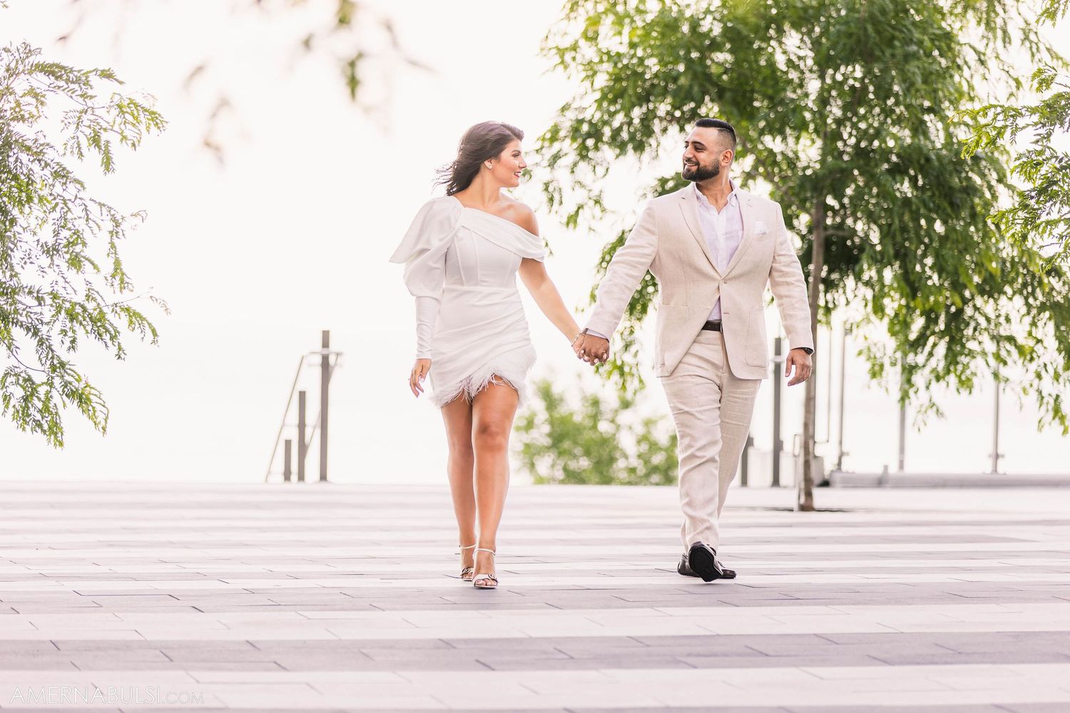 A couple in light-colored outfits holding hands while walking up outdoor stone steps.
