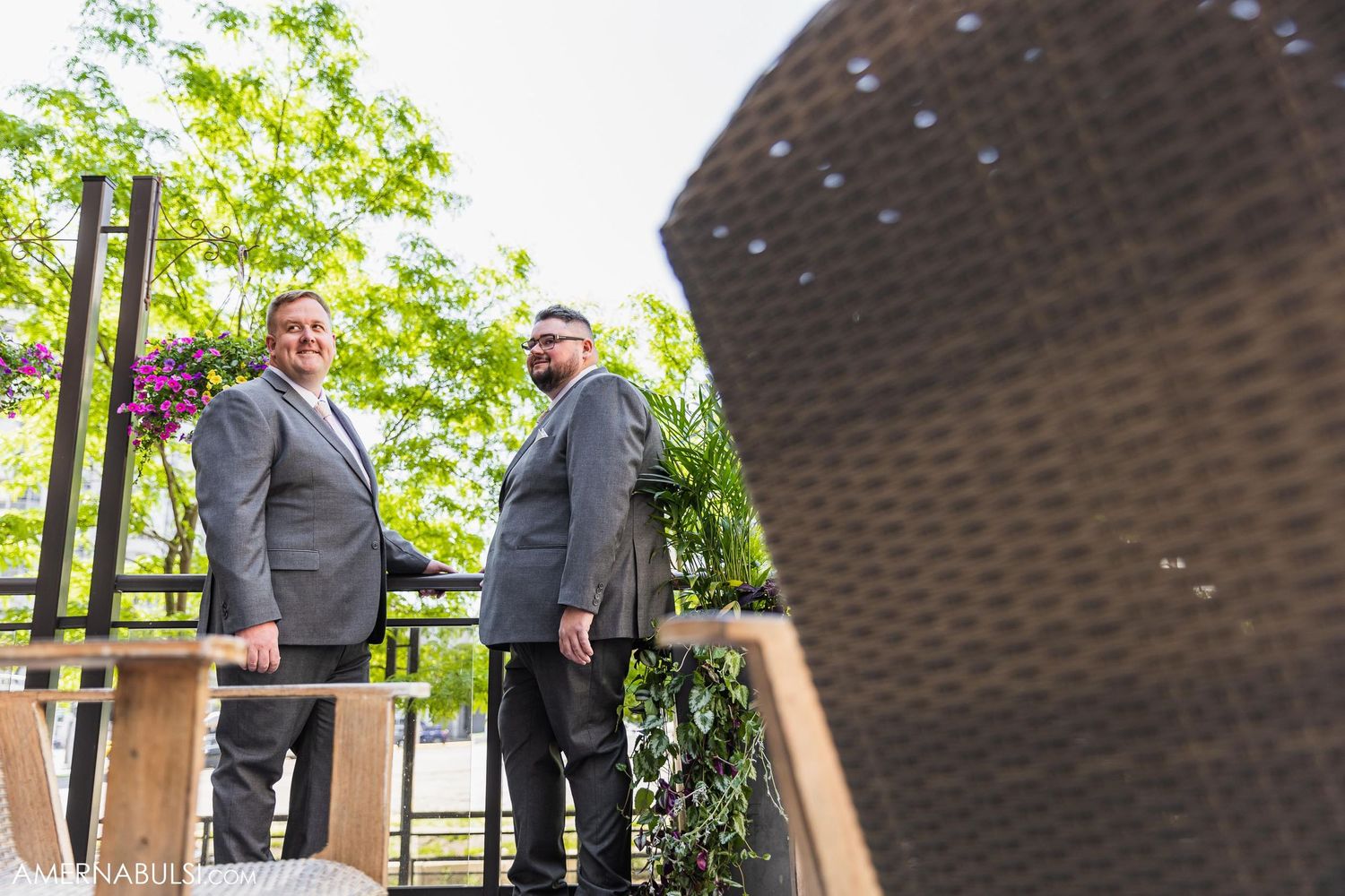 Two groomsmen in matching gray suits standing on outdoor wooden deck.