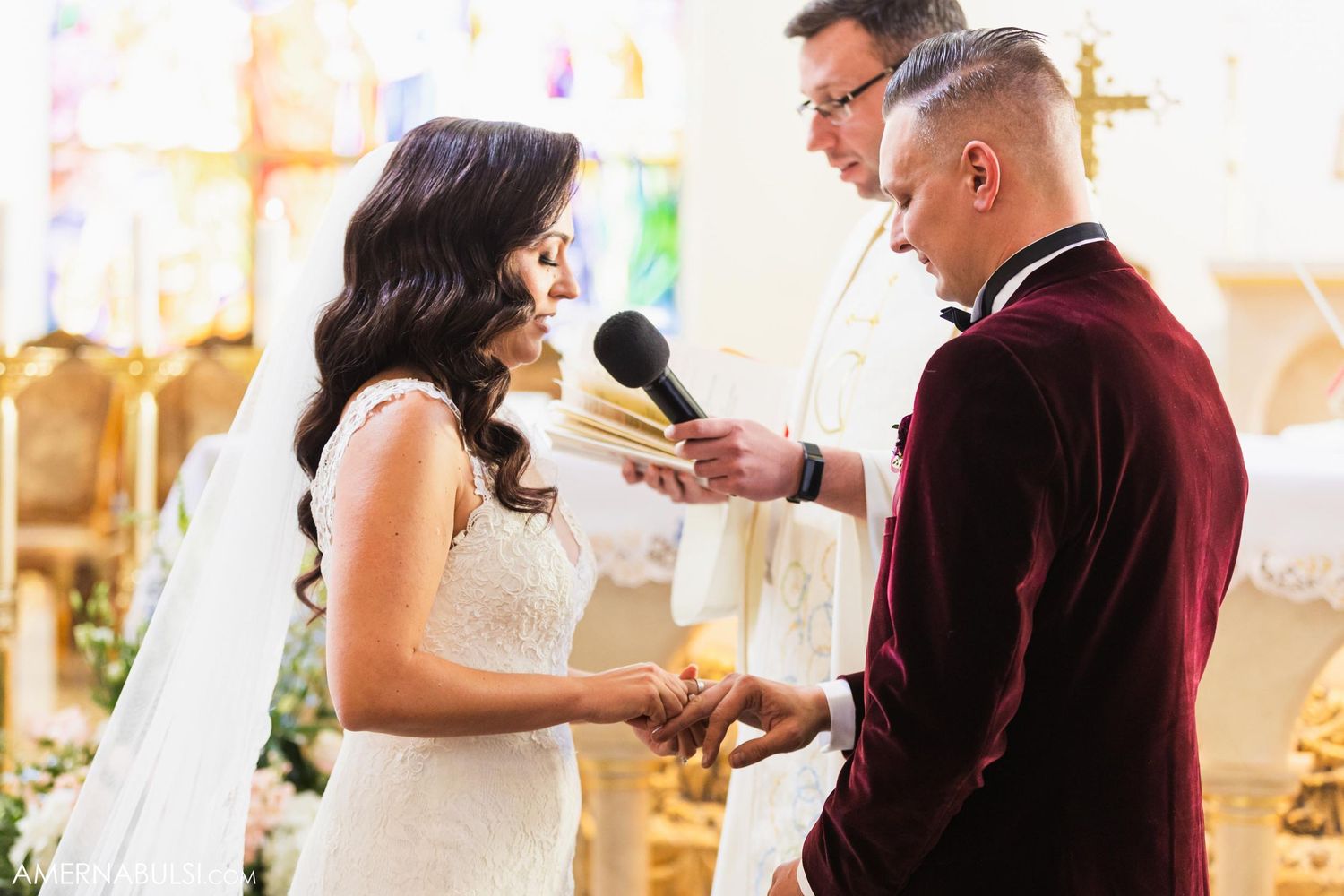 A couple exchanges rings during their wedding ceremony at a decorated church altar.