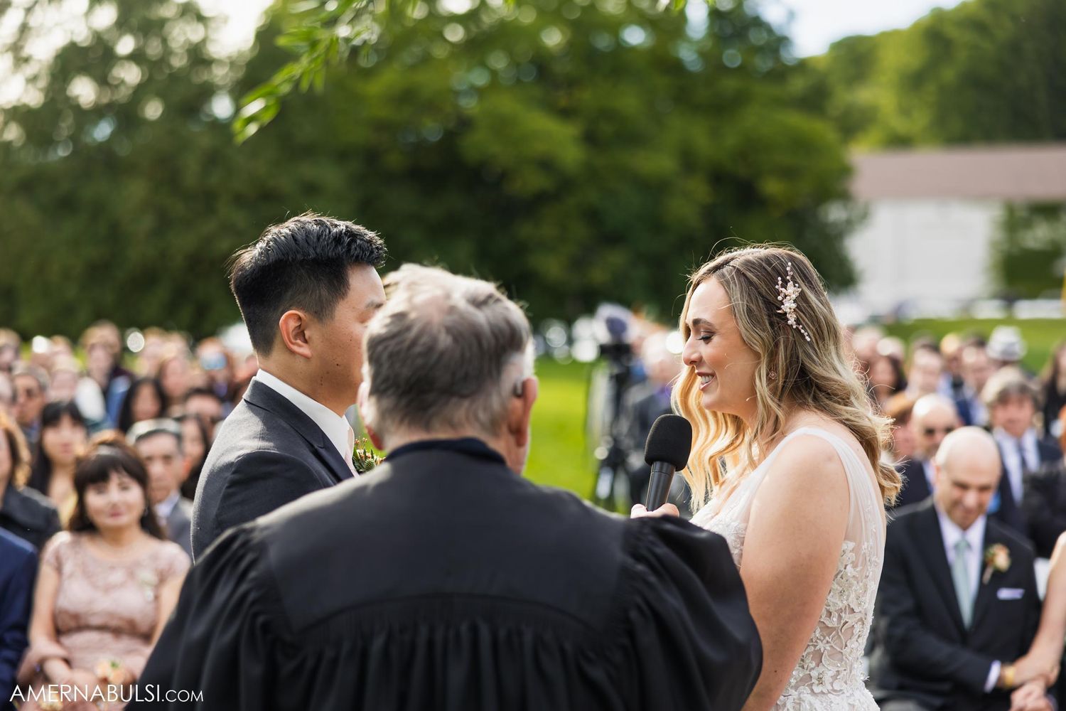 An intimate outdoor wedding ceremony moment captured with guests watching in the background.