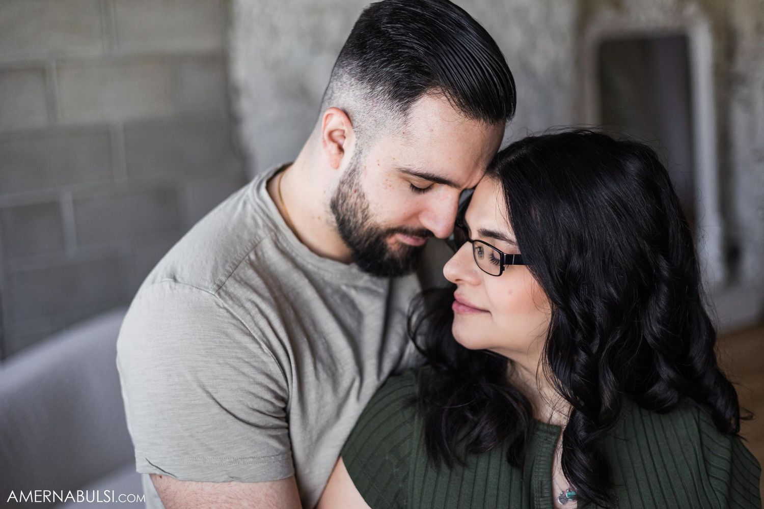 Romantic indoor maternity portrait against industrial brick wall backdrop.