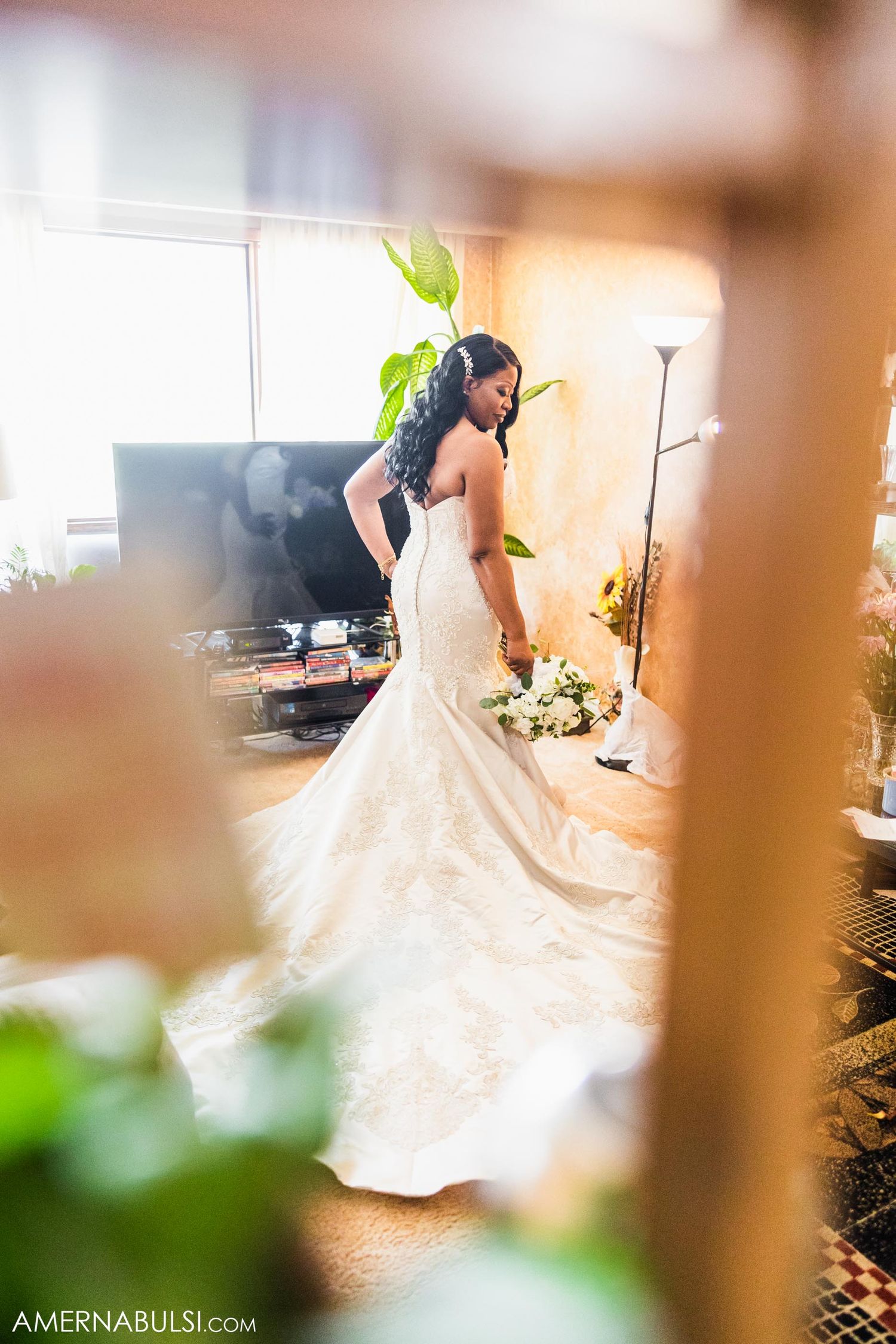 A stunning mermaid-style wedding dress is showcased in a softly lit room with delicate details and flowing train.