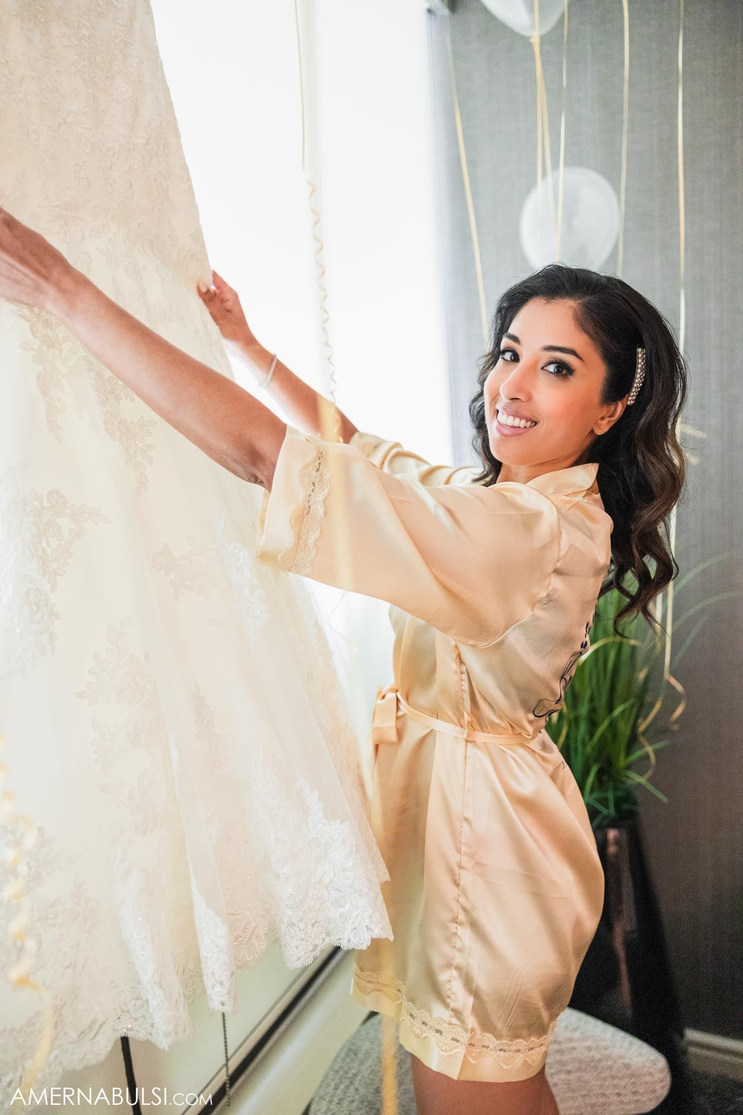 Bridal preparation moment with champagne colored silk robe and white wedding dress.