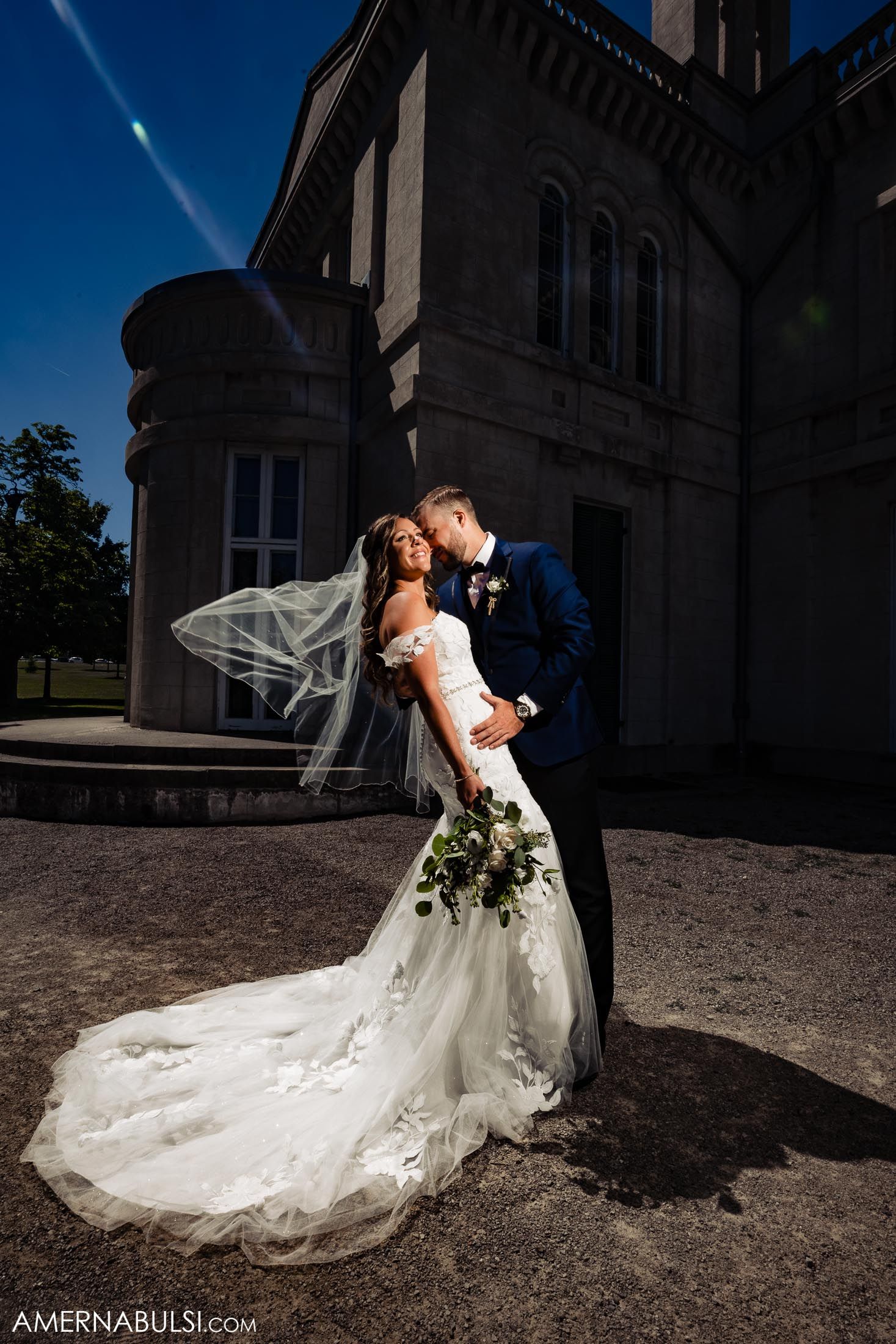Dramatic dip kiss portrait against gothic architecture with flowing veil.