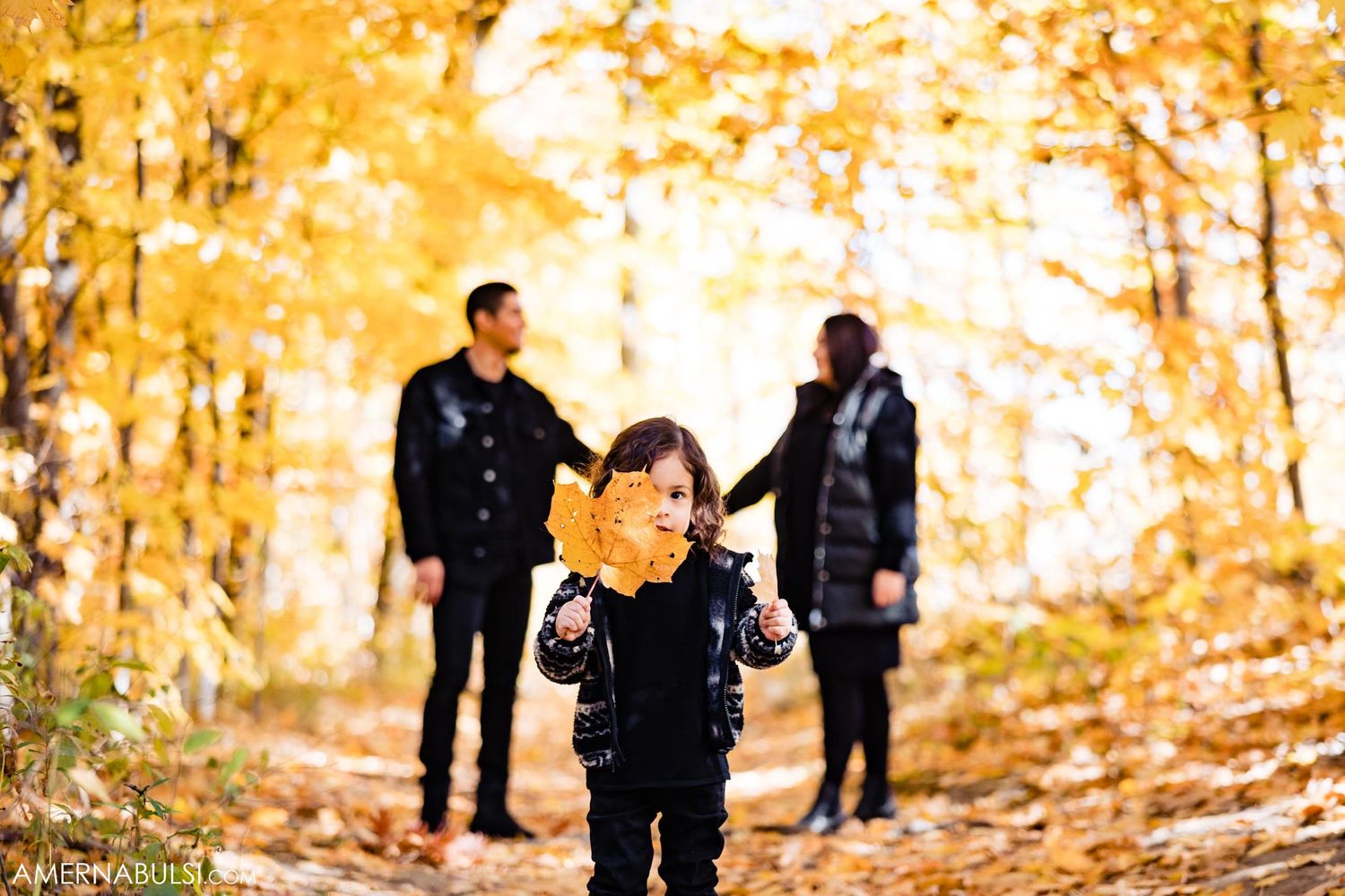 A small child in dark clothing explores a golden autumn forest path.